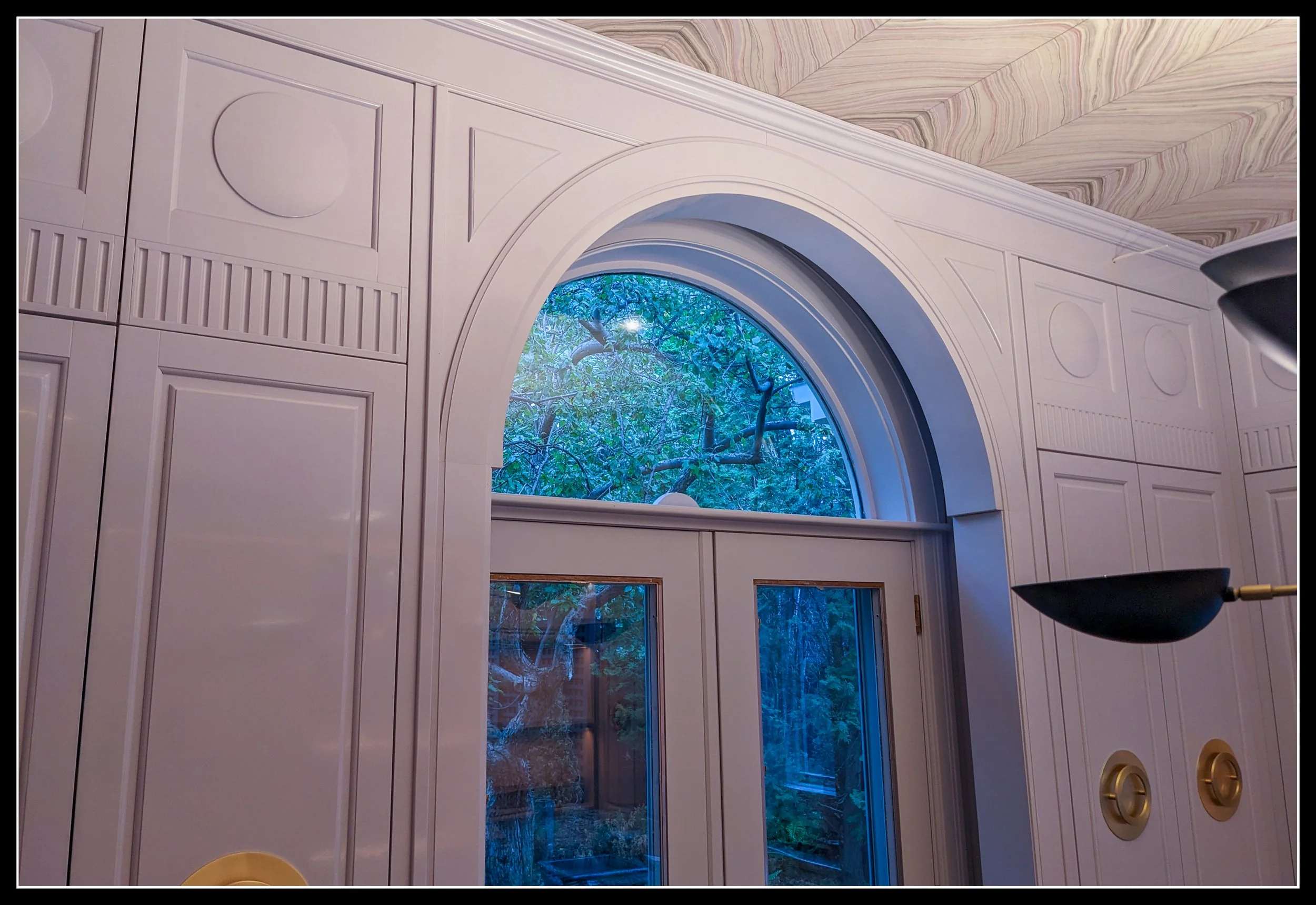 Grey gloss‑painted arched doorway with glass double doors and paneled wall detailing, showcasing high‑skill cabinetry and precision finishing.