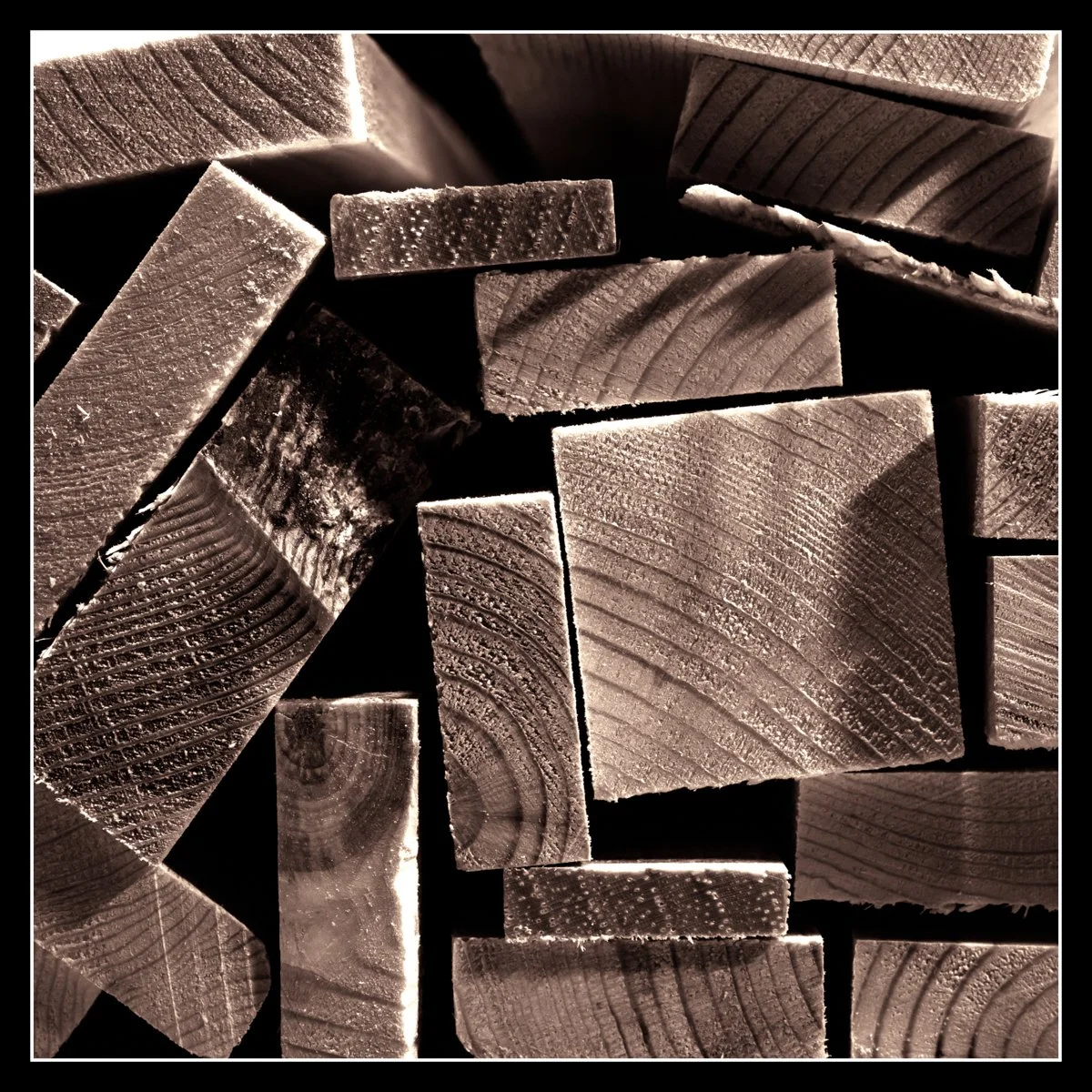 Hardwood off‑cuts — walnut, maple, oak, elm — stacked tightly, showing grain and texture before becoming end‑grain cutting boards.