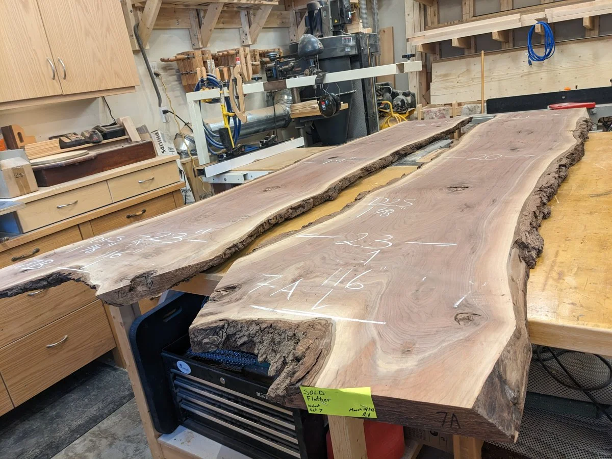 Pair of bookmatched walnut live‑edge slabs on a woodworking bench, showing mirrored grain and natural bark edges.
