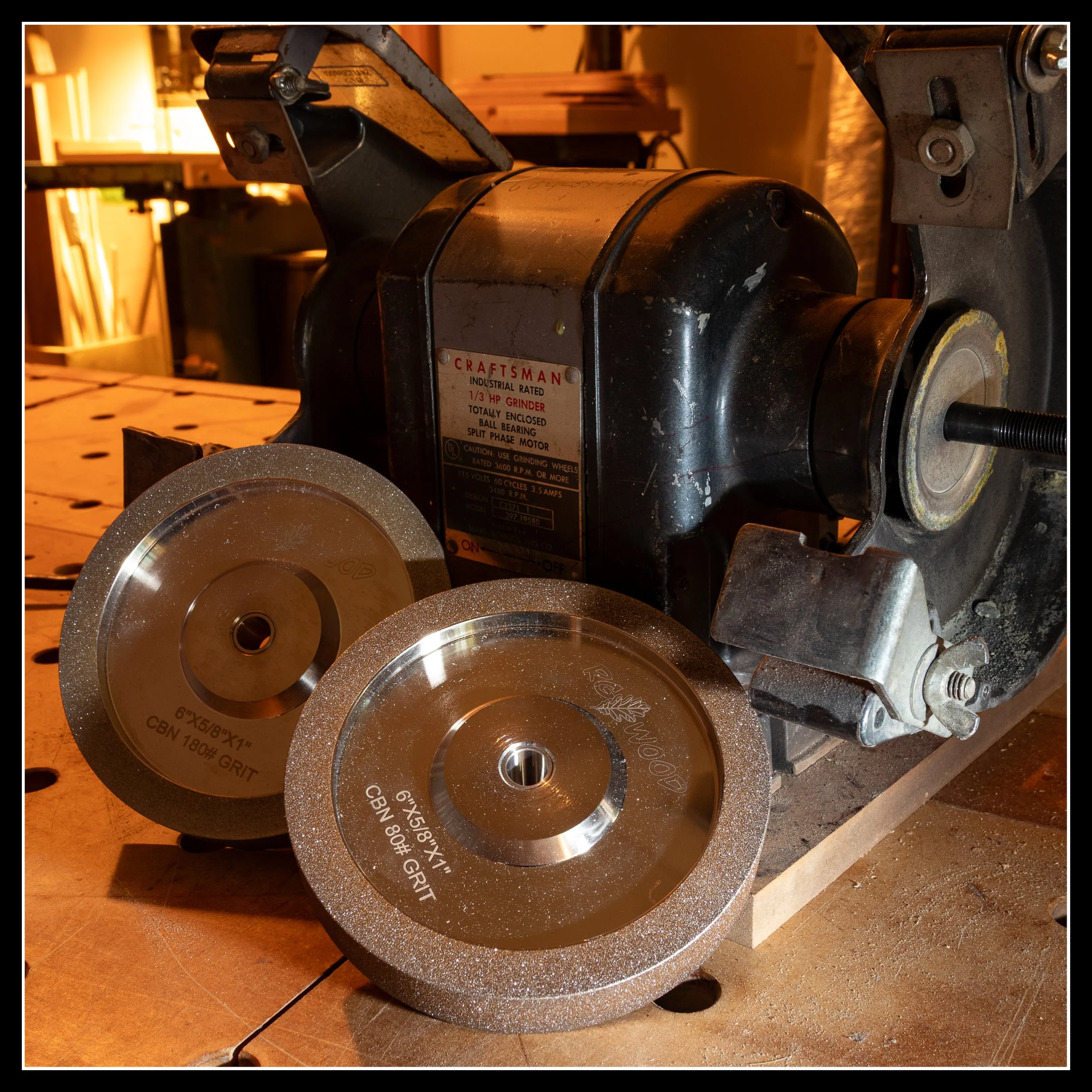 A Craftsman bench grinder fitted with 6‑inch CBN wheels sitting on a woodworking bench, showing the setup used for sharpening in the shop.
