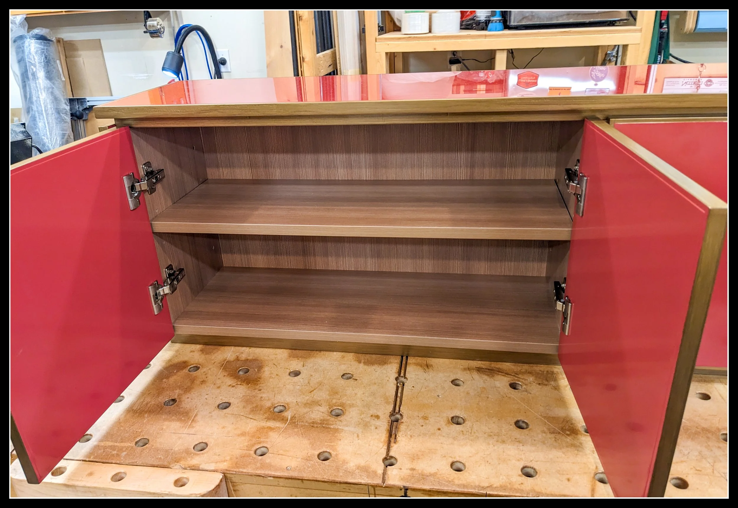 Open gloss‑red console showing internal cabinet structure, shelves, and joinery — the bones that support walnut accents and brass hardware.