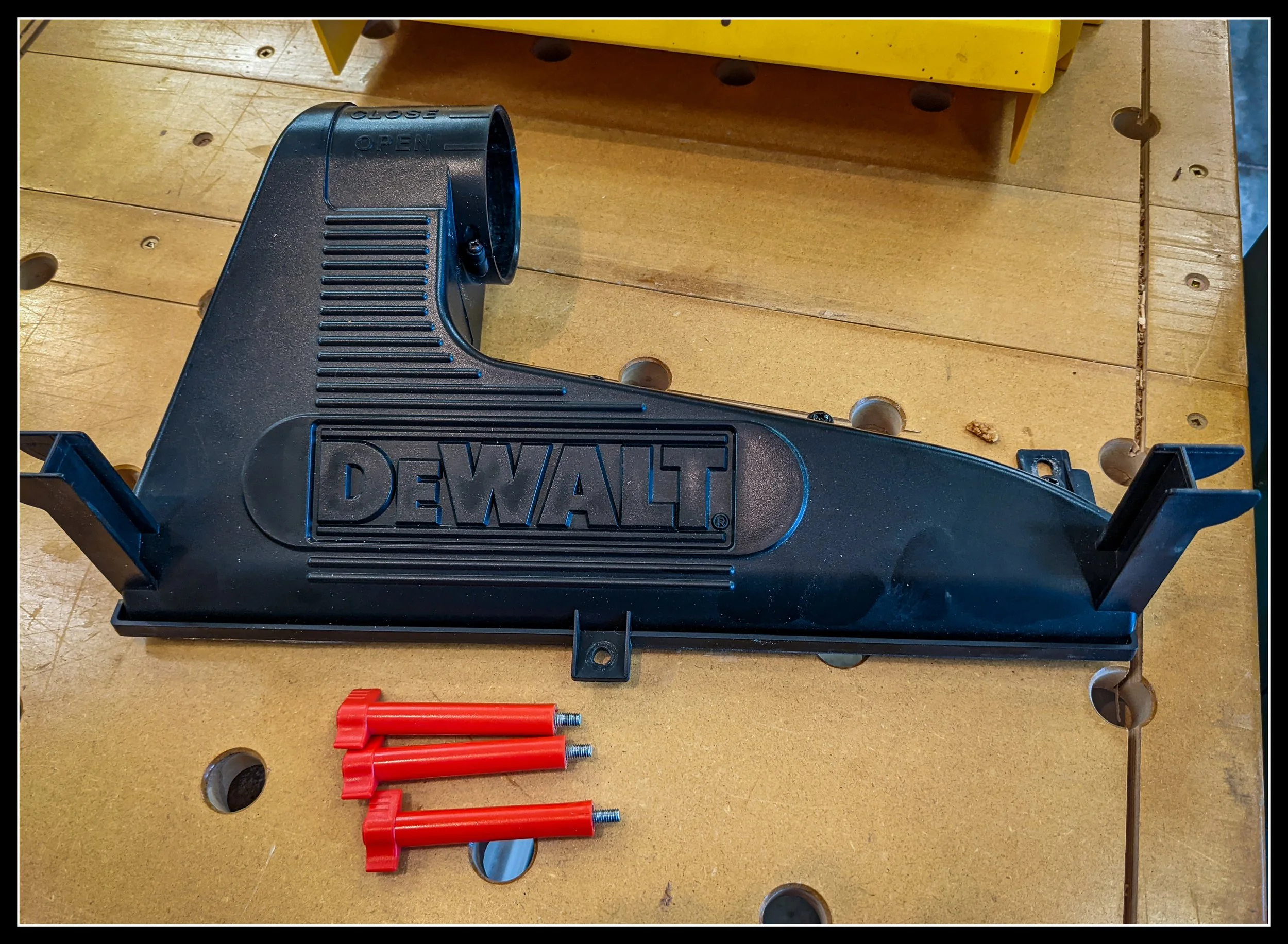 DeWalt DW735 dust‑ejection housing on a workbench, showing cracked plastic port and mounting tabs with red alignment pins nearby.
