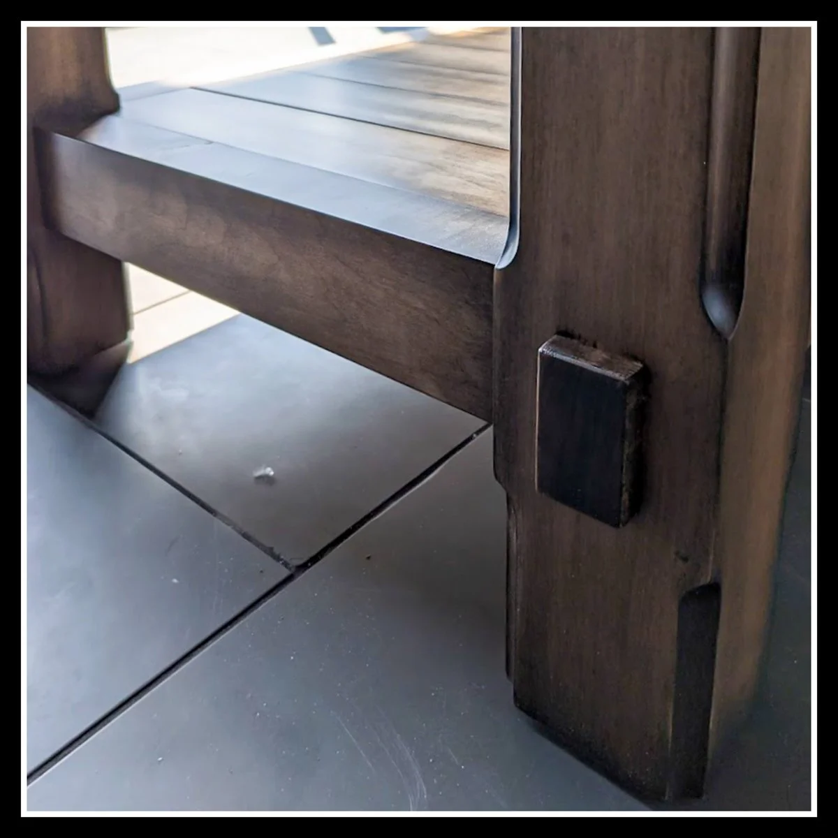 A close-up of a maple table corner showing the joint details and a section of the tiled floor beneath.