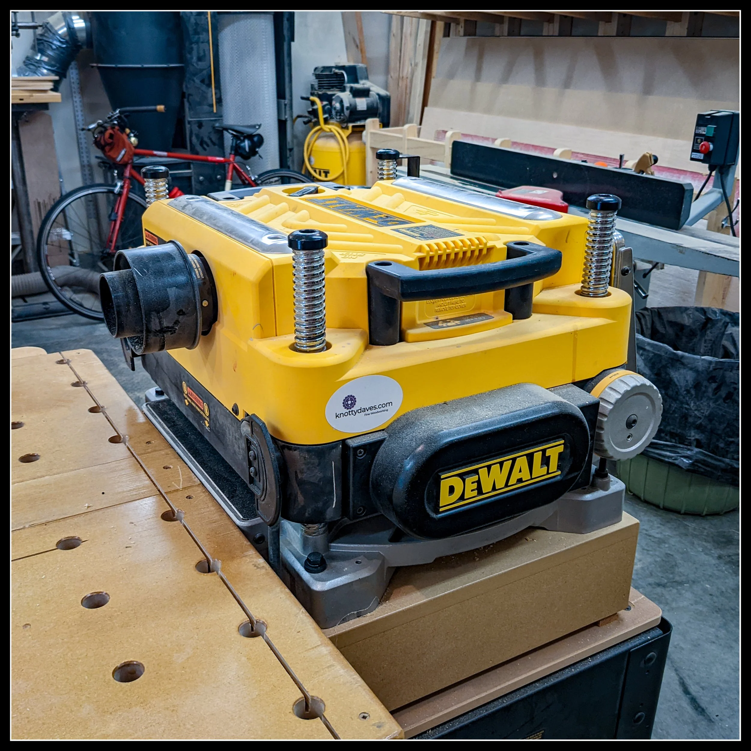 DeWalt DW735 13-inch thickness planer on a woodworking bench, showing chrome elevation posts, dust port, and knottydaves.com sticker, surrounded by shop tools.