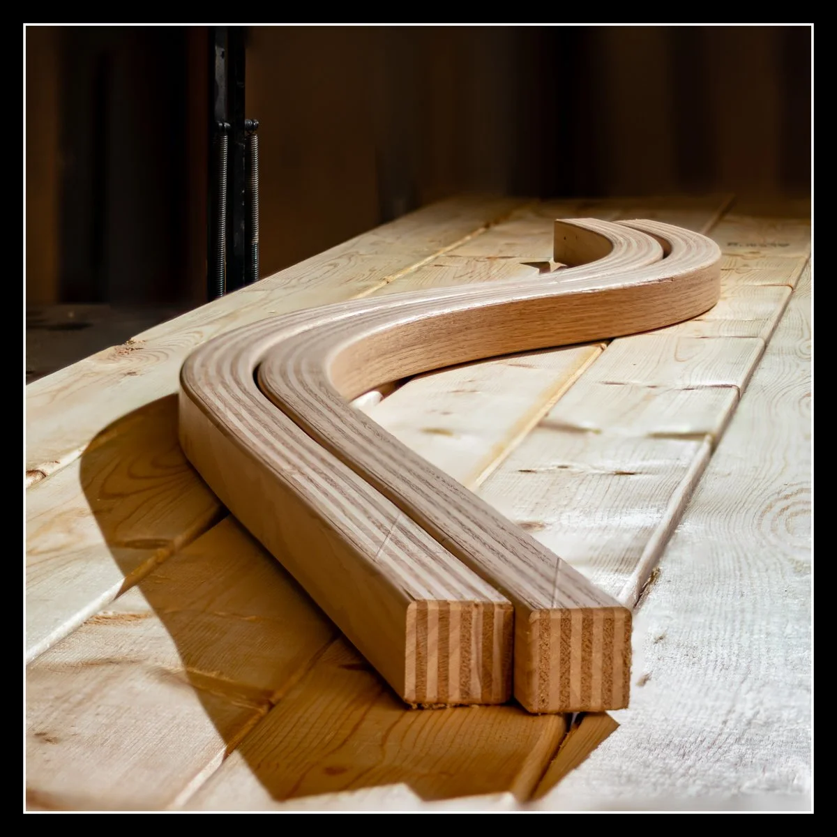 A wooden curved piece on a light wooden workbench in a woodworking shop.