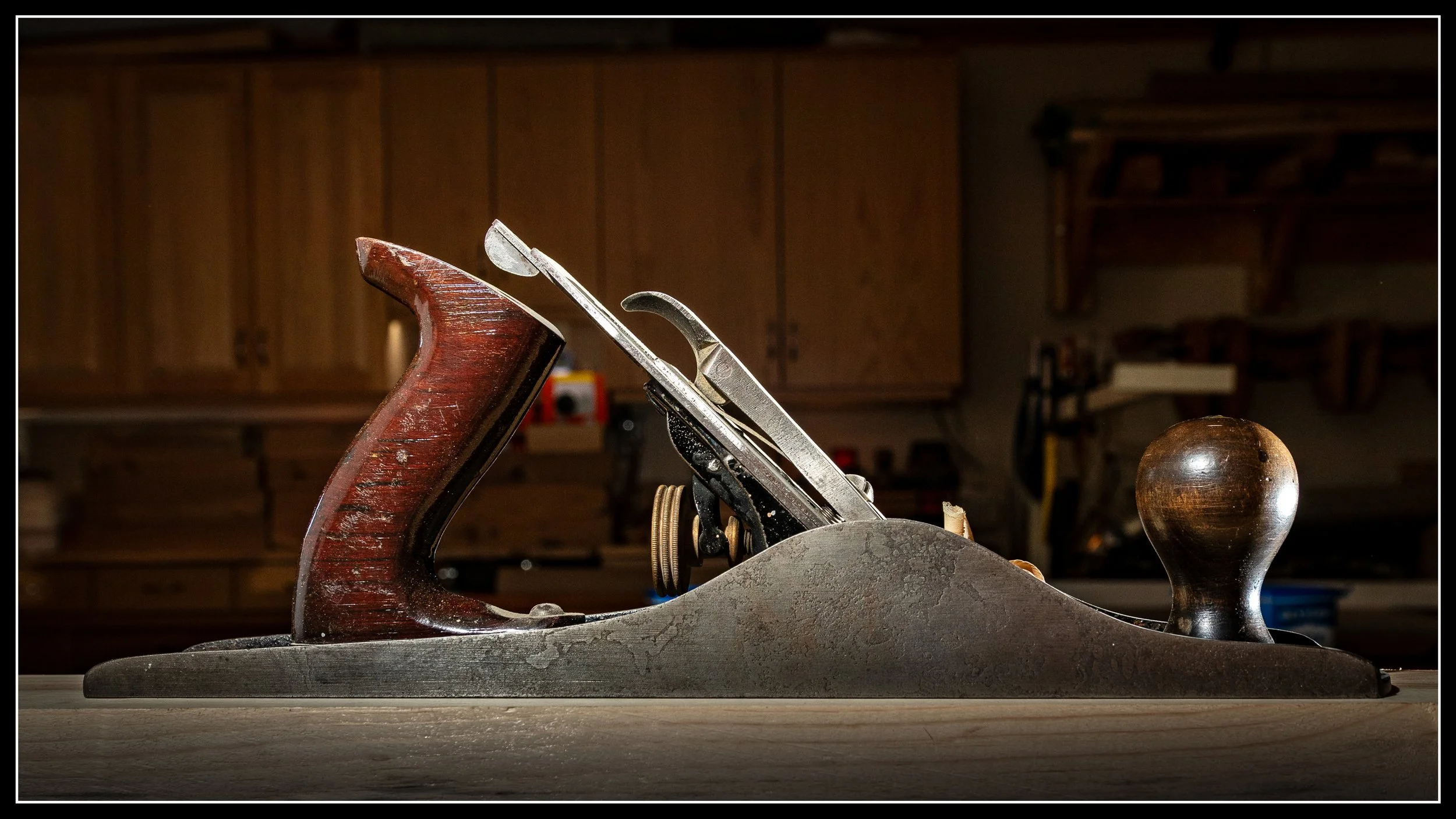 A vintage hand plane woodworking tool with a wooden handle and metal blade, placed on a wooden surface in a workshop setting.