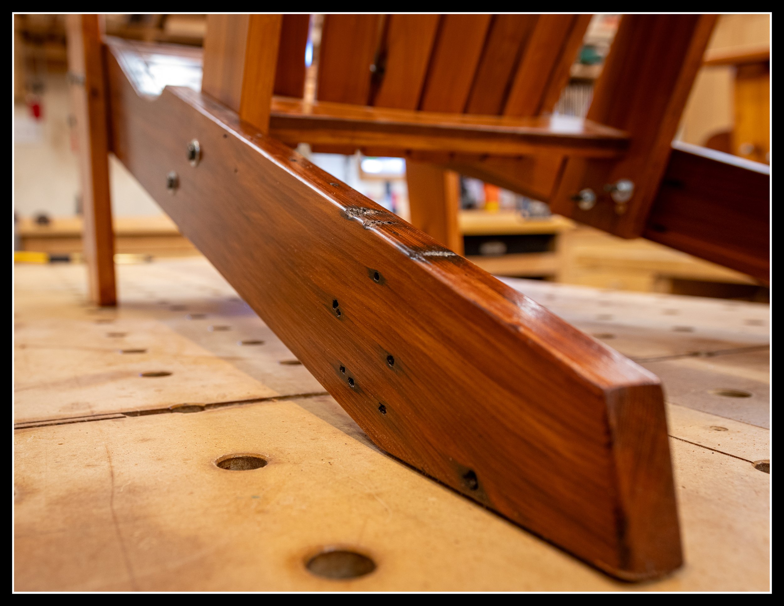 Close-up of a wooden chair leg standing on a workbench in a woodworking shop.