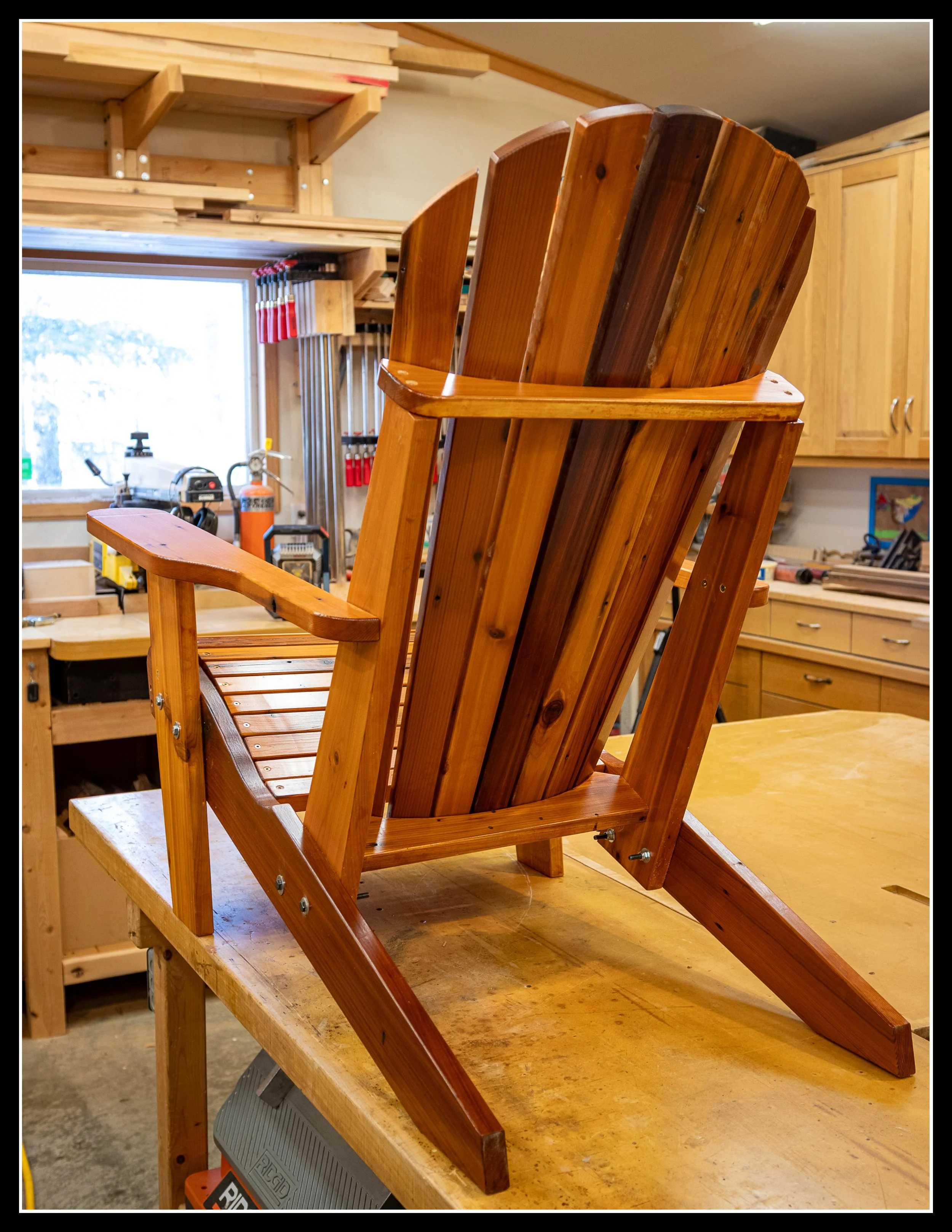 A wooden Adirondack chair on a workbench in a woodworking shop.