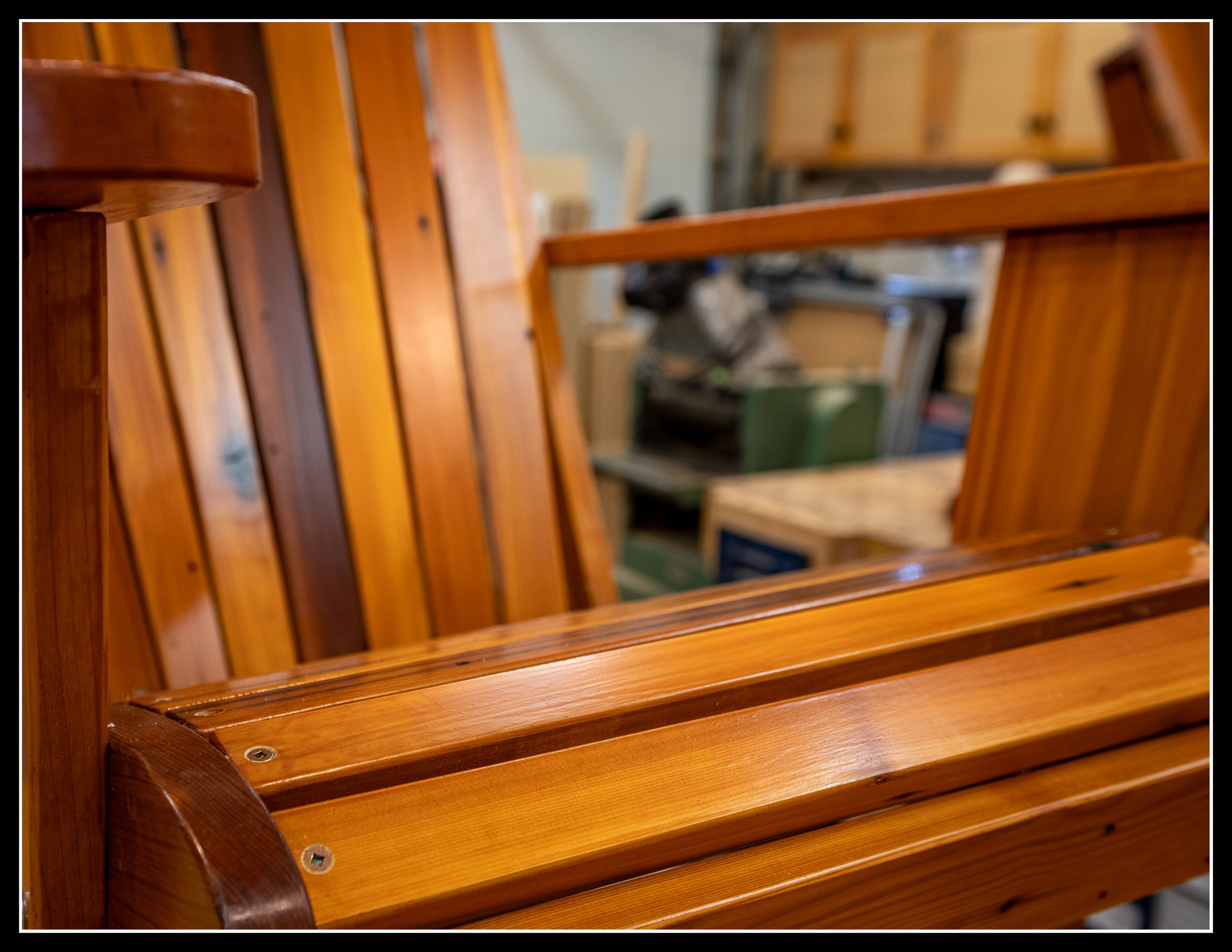 A close-up of a wooden chair with vertical slats and armrests, showing a polished finish with a warm wood tone.