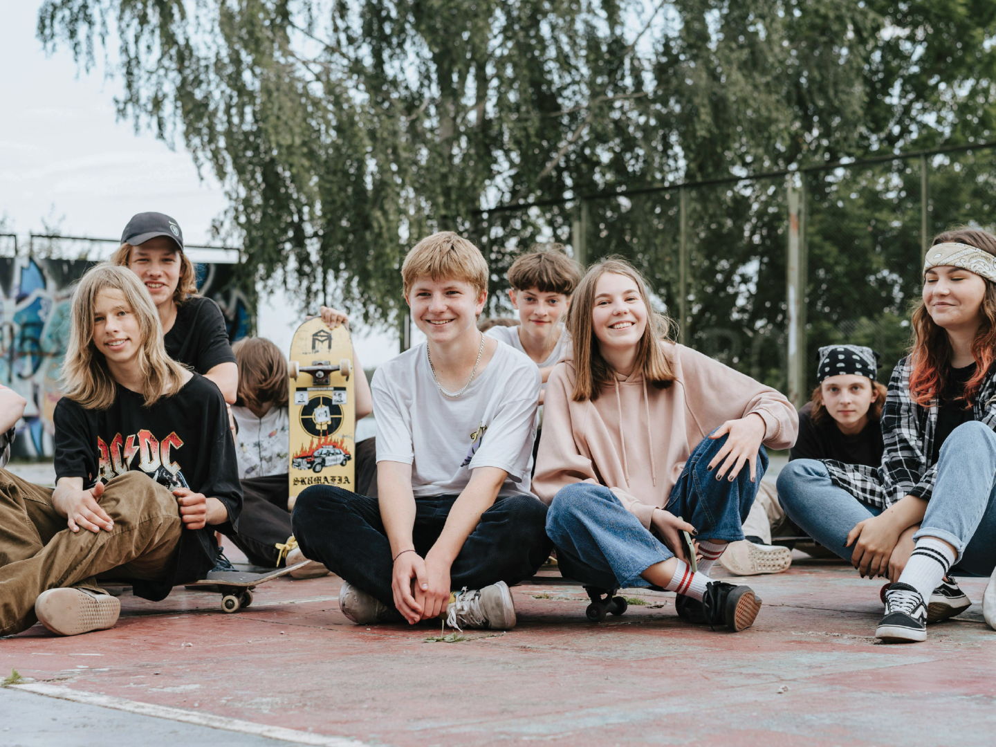 Group of teenagers sitting on skate court with skateboards, smiling and enjoying hanging out outdoors.