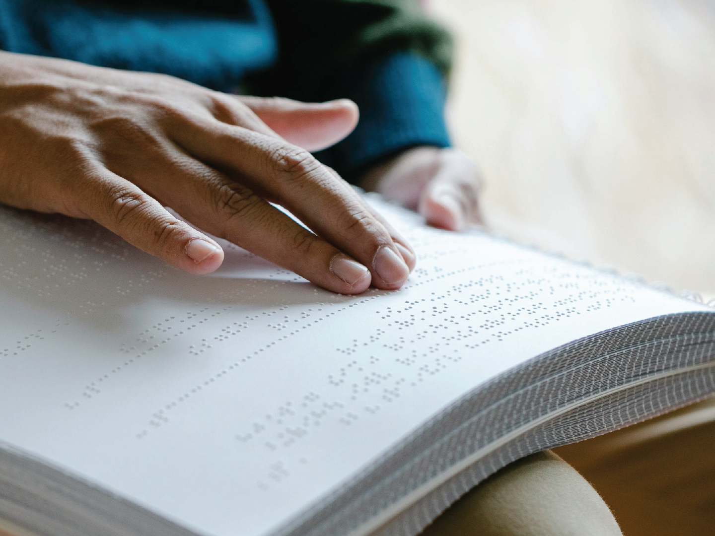 Close-up of a person's hand reading Braille on an open book.