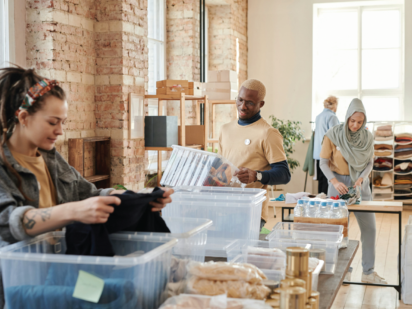 People sorting and packing items in a well-lit, industrial-style room with exposed brick walls and large windows.