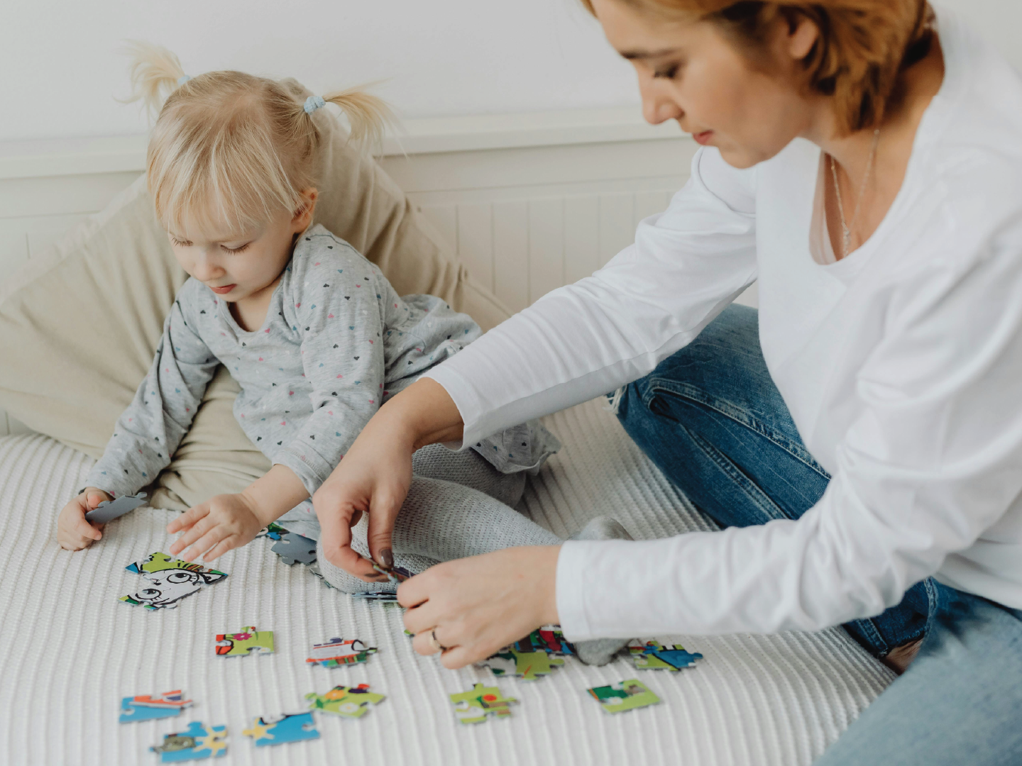 Young girl and woman assembling a colorful puzzle on a bed, focusing on the puzzle pieces.
