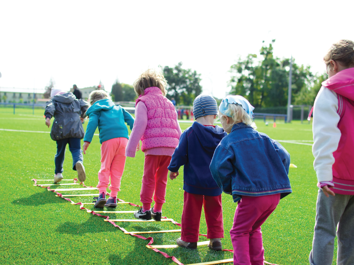 Children participating in an outdoor training exercise on a grassy field using an agility ladder.