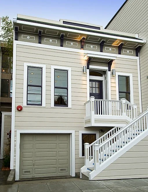Modern multi-story house with a garage, staircase, and balcony, featuring beige siding and dark window frames.