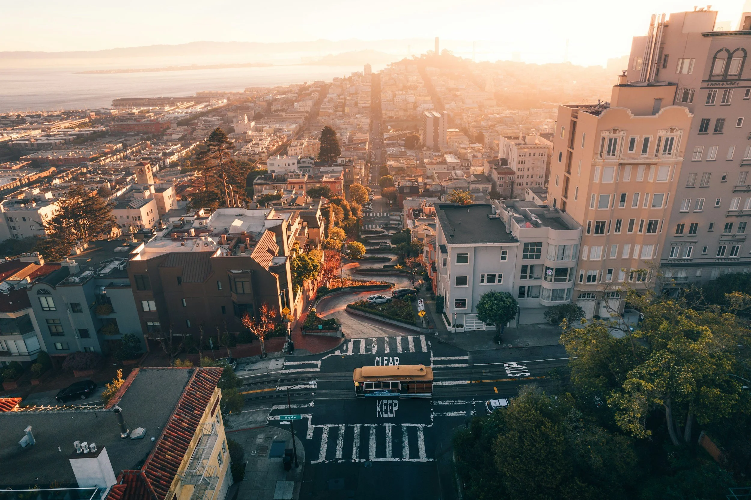Aerial view of a San Francisco city street with a trolley, crosswalks, and surrounding residential buildings during sunset.