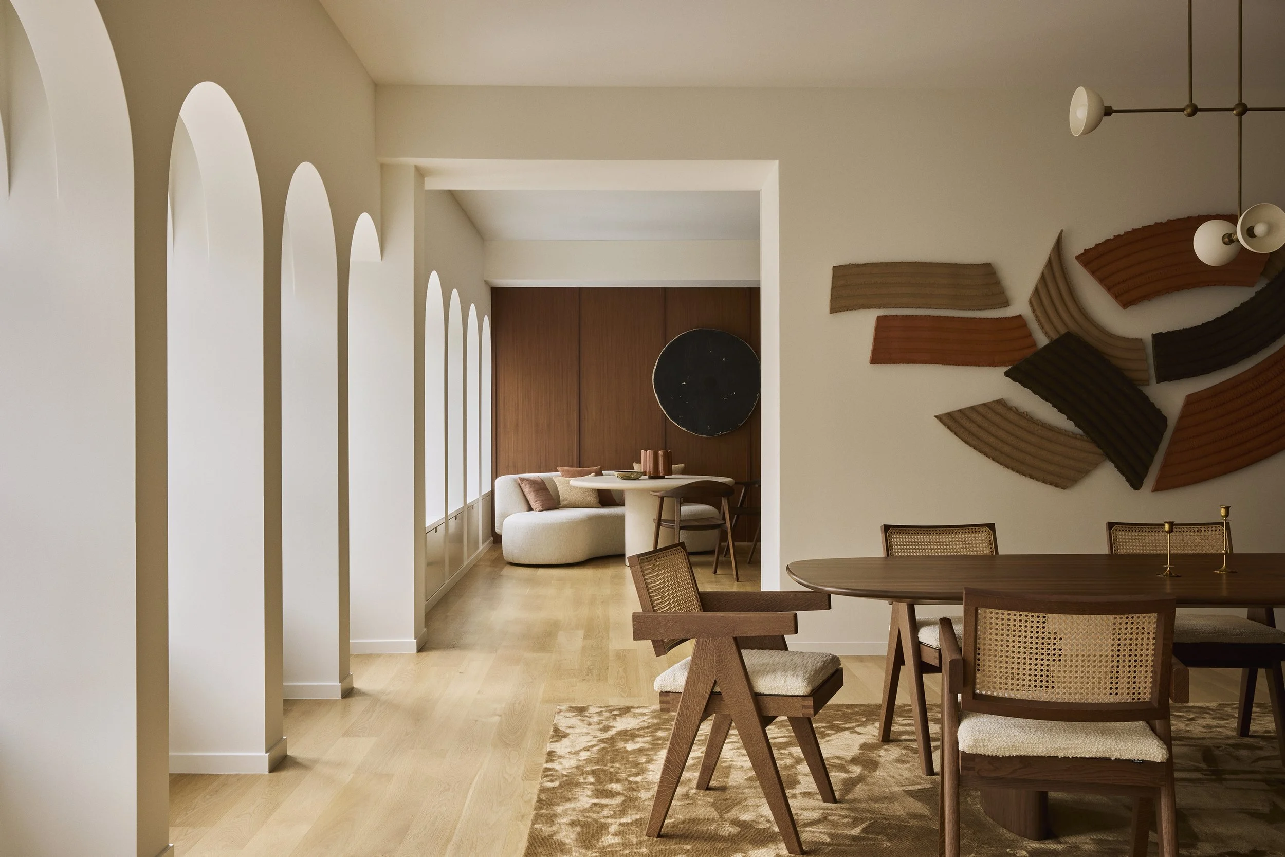 Modern dining room with wooden table and chairs, wall art with curved shapes, and a sitting area with a curved sofa and wooden accents.