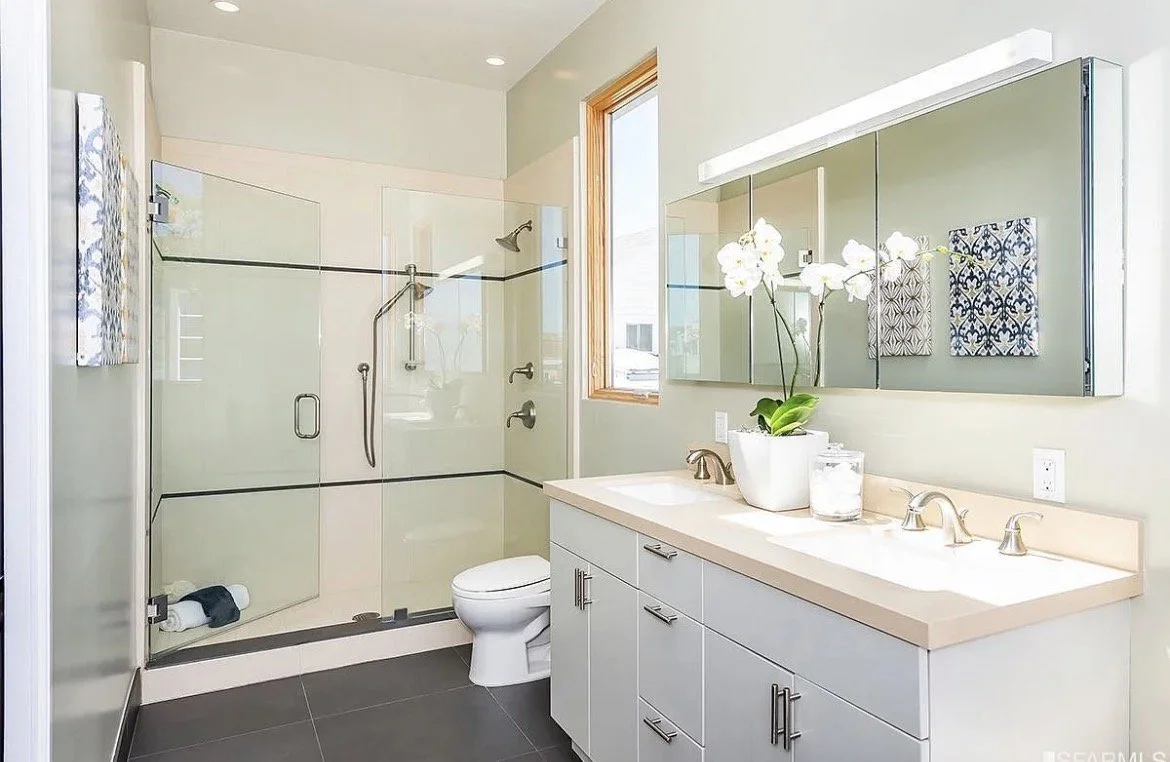 Modern bathroom with a glass-enclosed shower, a white vanity with a sink, a large mirror, a potted orchid, and neatly folded towels.