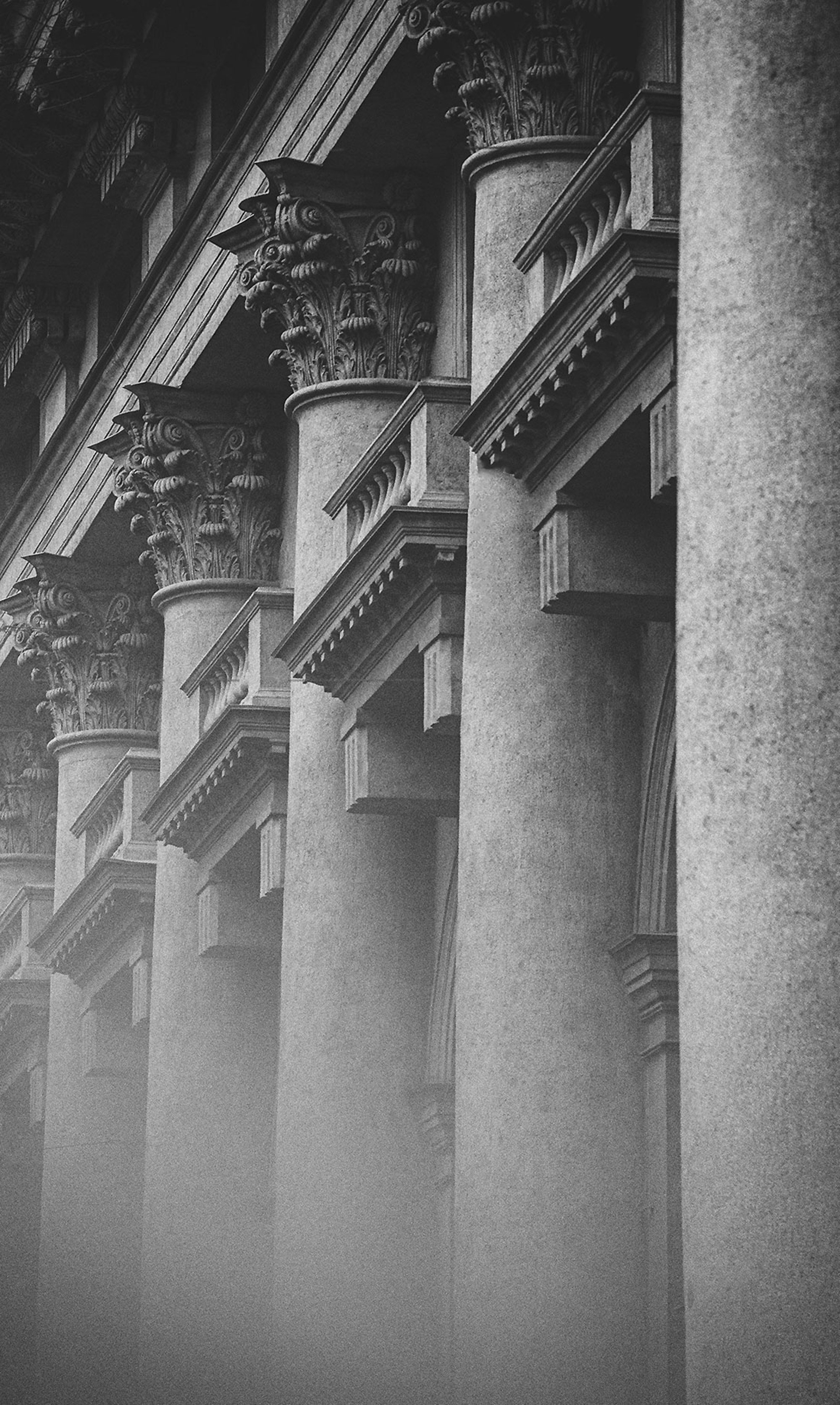 Close-up of classical architectural columns with ornate Corinthian capitals in black and white.