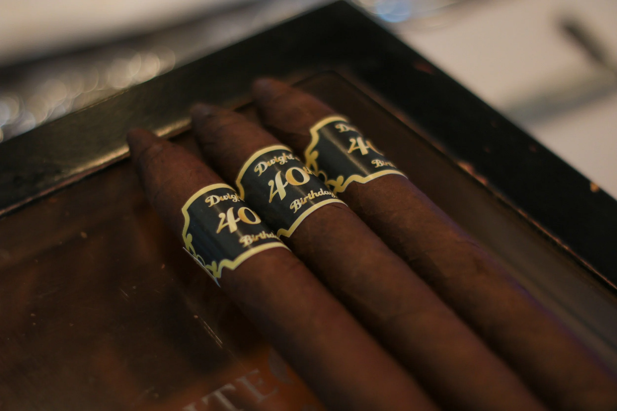 Three cigars with black and gold bands labeled 'Dough 40 Birthday' resting on a dark surface.
