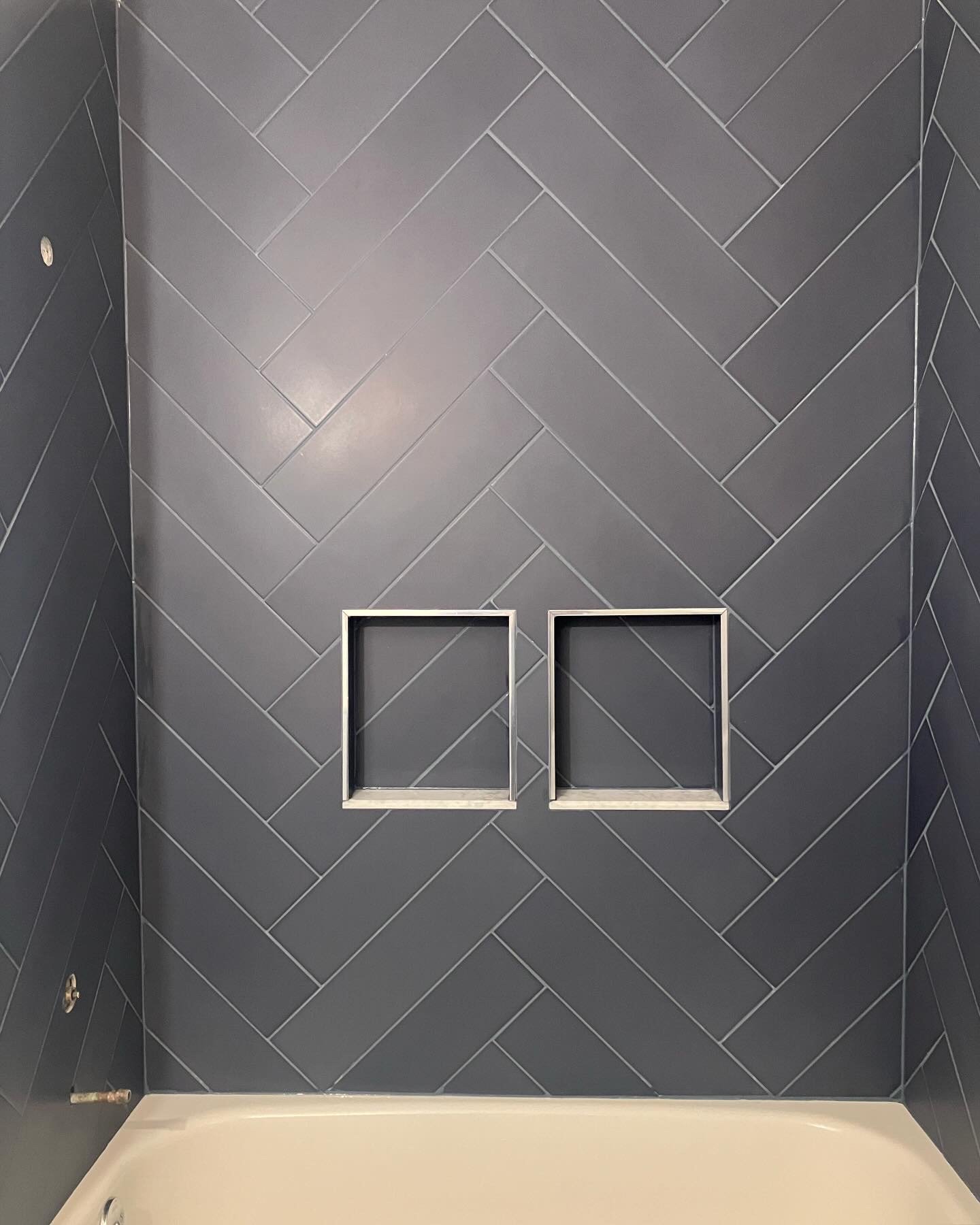 Interior shower wall with large gray herringbone tiles and two built-in square shelves.