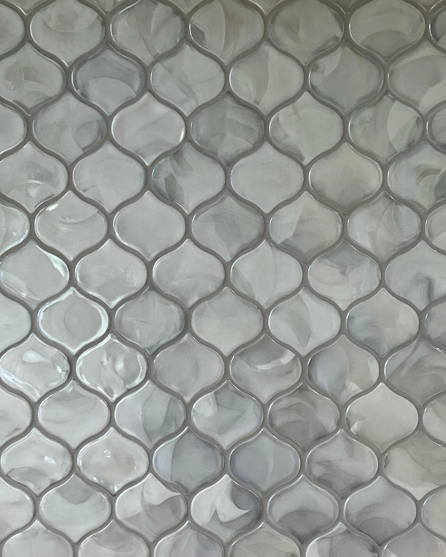 Close-up of a tile wall with shiny, marble-like, grayish-white mosaic tiles in a geometric pattern.