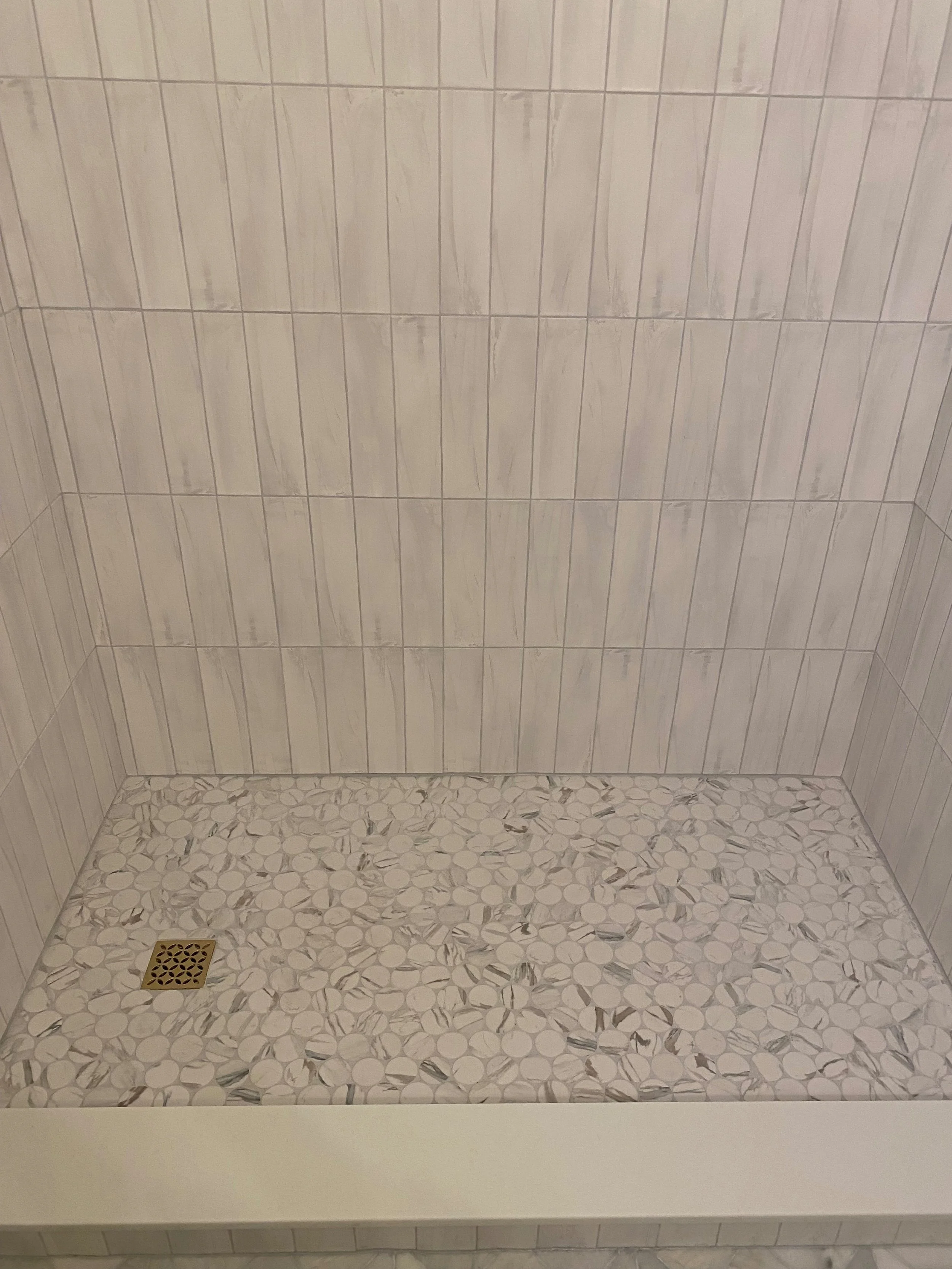 Empty shower with beige wall tiles, pebble-patterned floor tiles, and a gold drain cover.