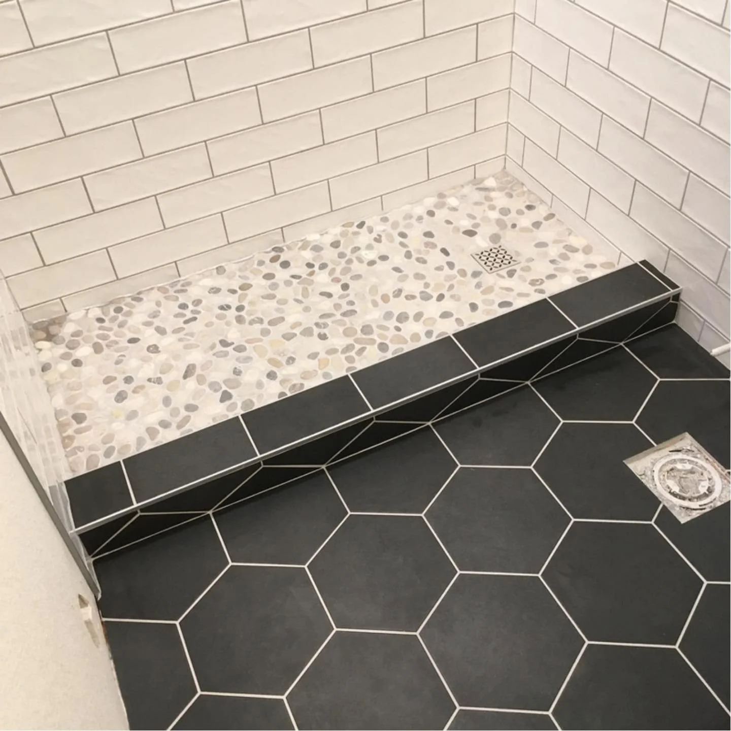 Tile shower floor with pebble design, black and white hexagon tile floor, and wall tiles with white subway style bricks.