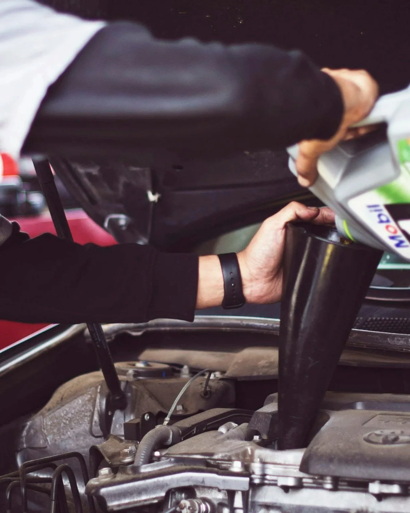 A person refilling the engine of a race car with oil in a garage.