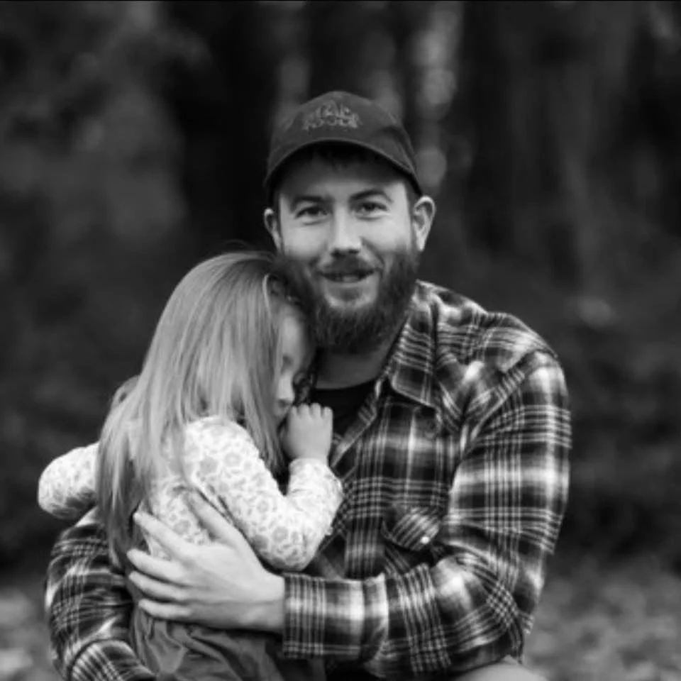 Man holding young girl close in an outdoor setting, with trees blurred in the background