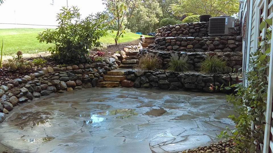 Backyard with stone landscaping, tiered rock formation with water features, small waterfall, and a slate patio in the foreground.
