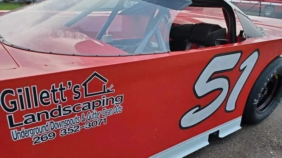 Racing car with number 51 and Gillett's Landscaping advertisement on the side, parked on asphalt.