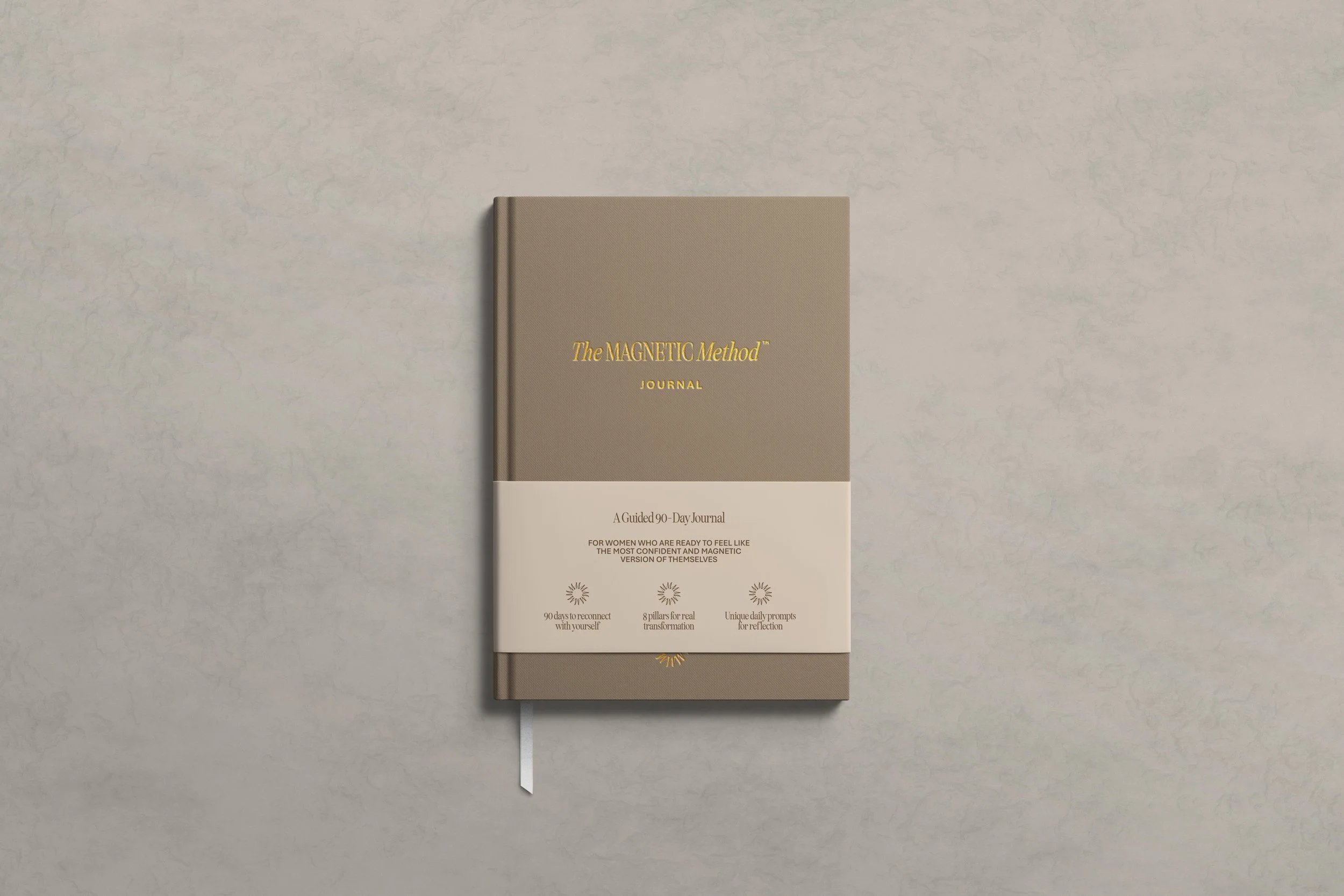 A 90-day guided journal titled 'The Magnetic Method' with a beige cover, gold lettering, and a white band around the middle with additional text and icons.