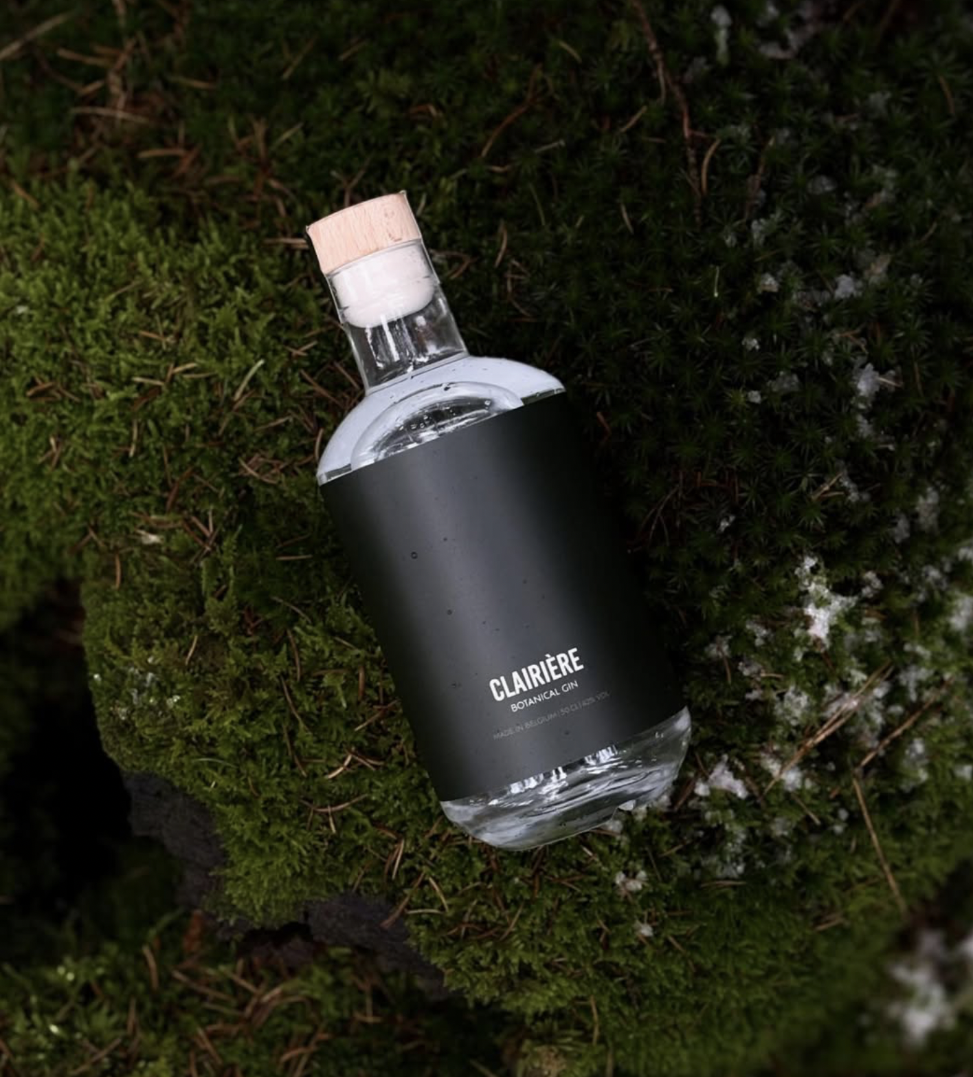 Une bouteille de gin botanique Clairière posée sur la mousse verte.