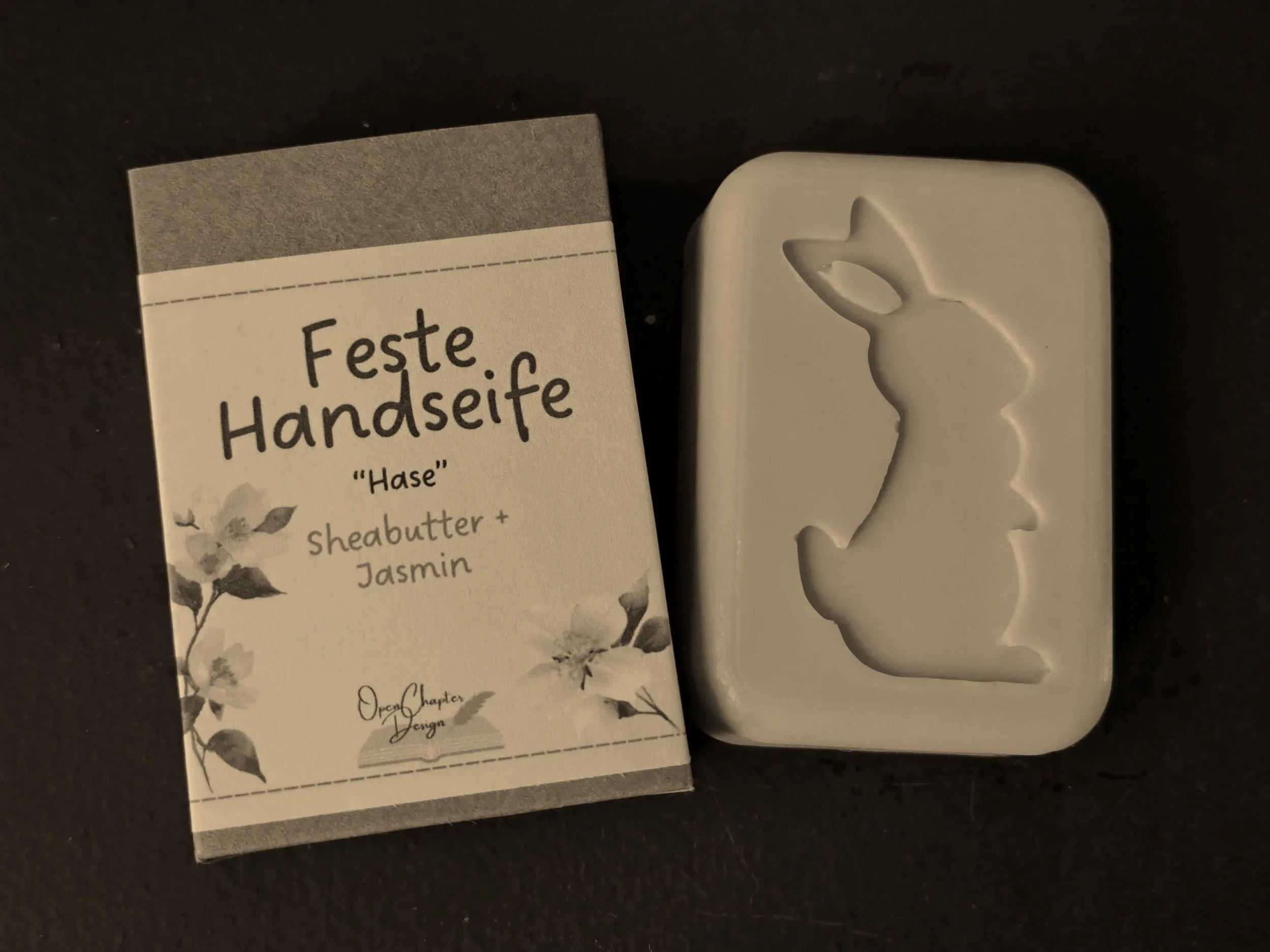 Seife in Hasenform neben Verpackung, die 'Feste Handseife' auf Deutsch schreibt, mit Thementext 'Hase', und enthält Sheabutter und Jasmin.