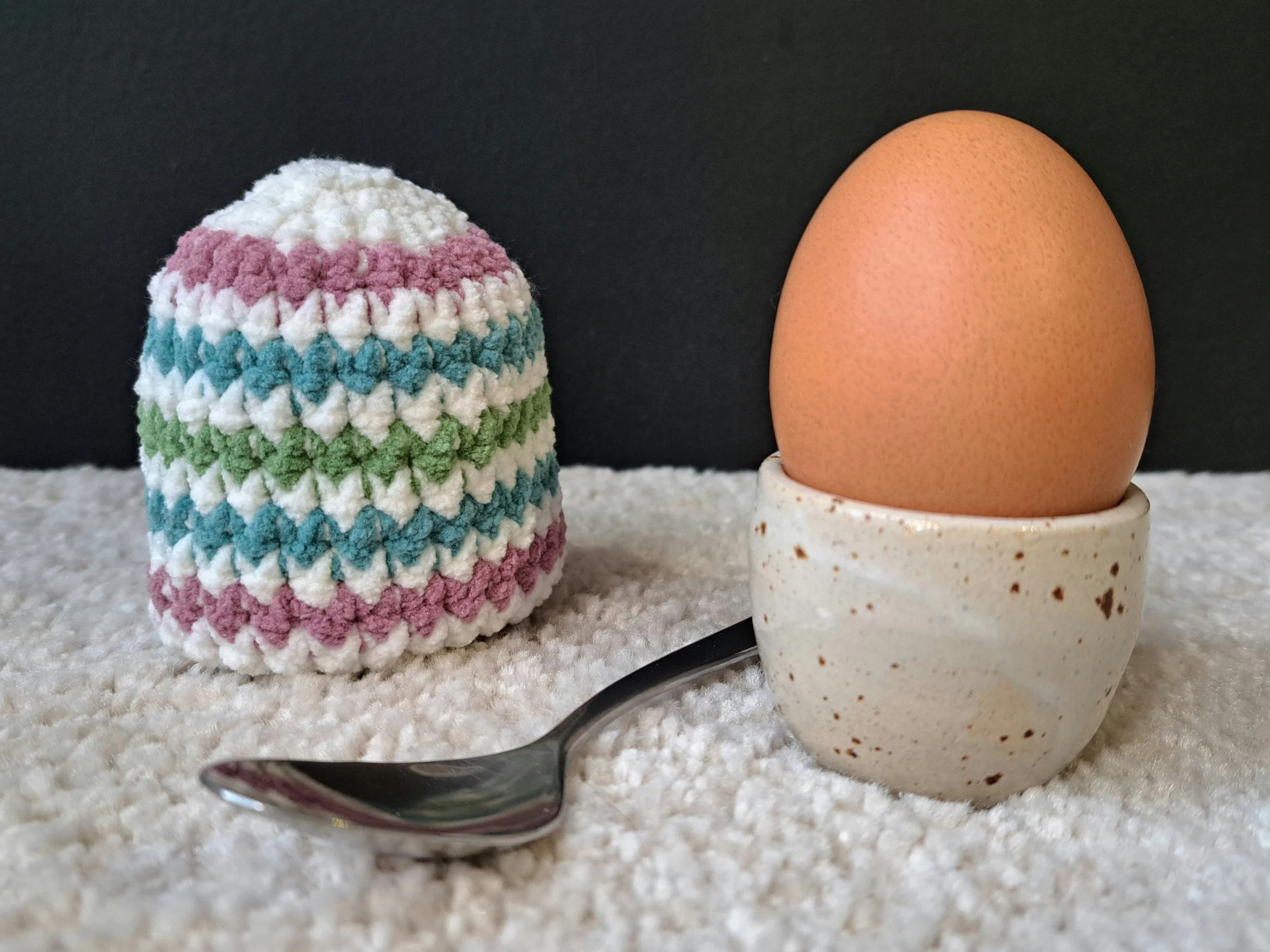 Eierwärmer "Osterei" steht auf dem Boden, rechts ist ein ei in einem Eierbecher von Töpferhof Ulrike Rost zusehen