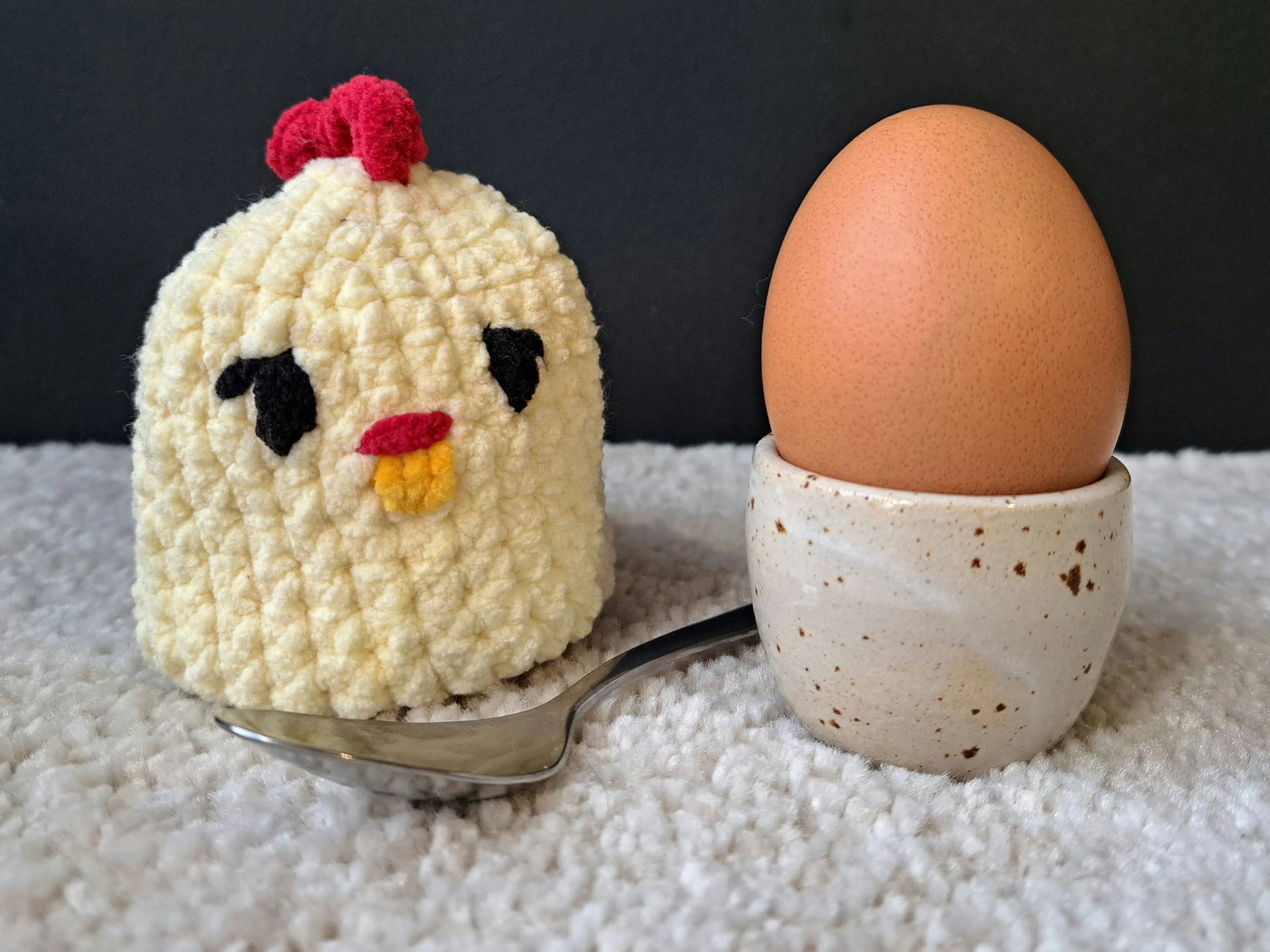 Eierwärmer "Kücken" steht auf dem Boden, rechts ist ein ei in einem Eierbecher von Töpferhof Ulrike Rost zusehen