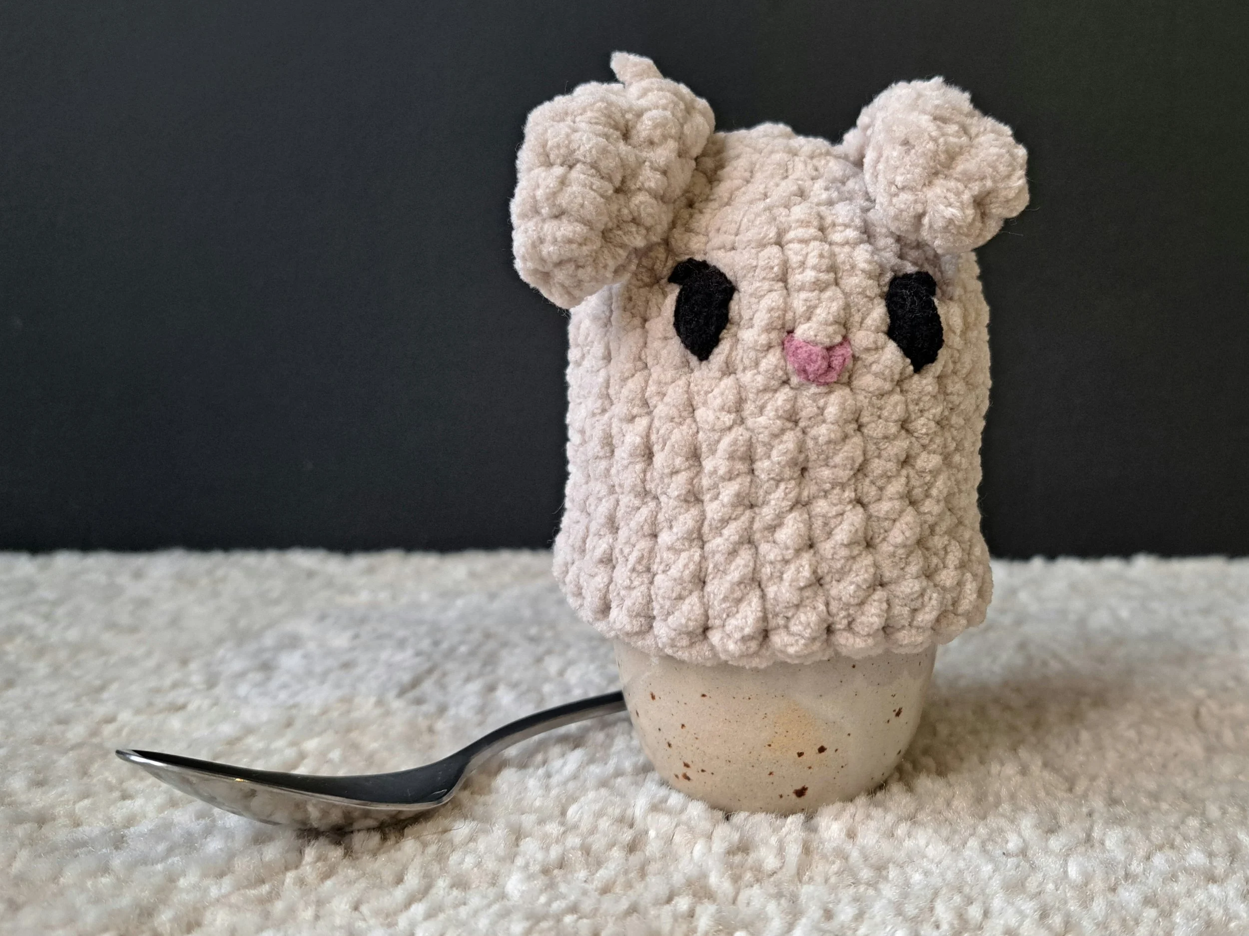 Eierwärmer "Hase hell" über ein Ei gestülpt, welches in einem Eierbecher steht, vor schwarzem Hintergrund