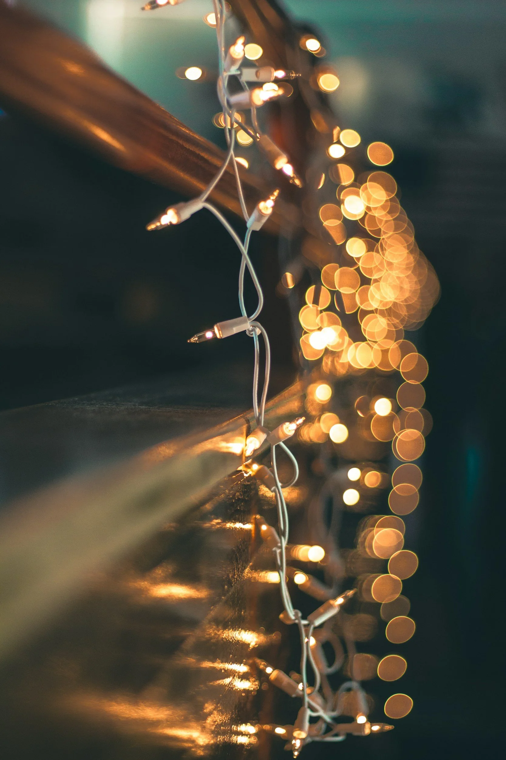 Close-up of warm white string lights hanging on a wooden surface, with a blurred background of bokeh light effects.