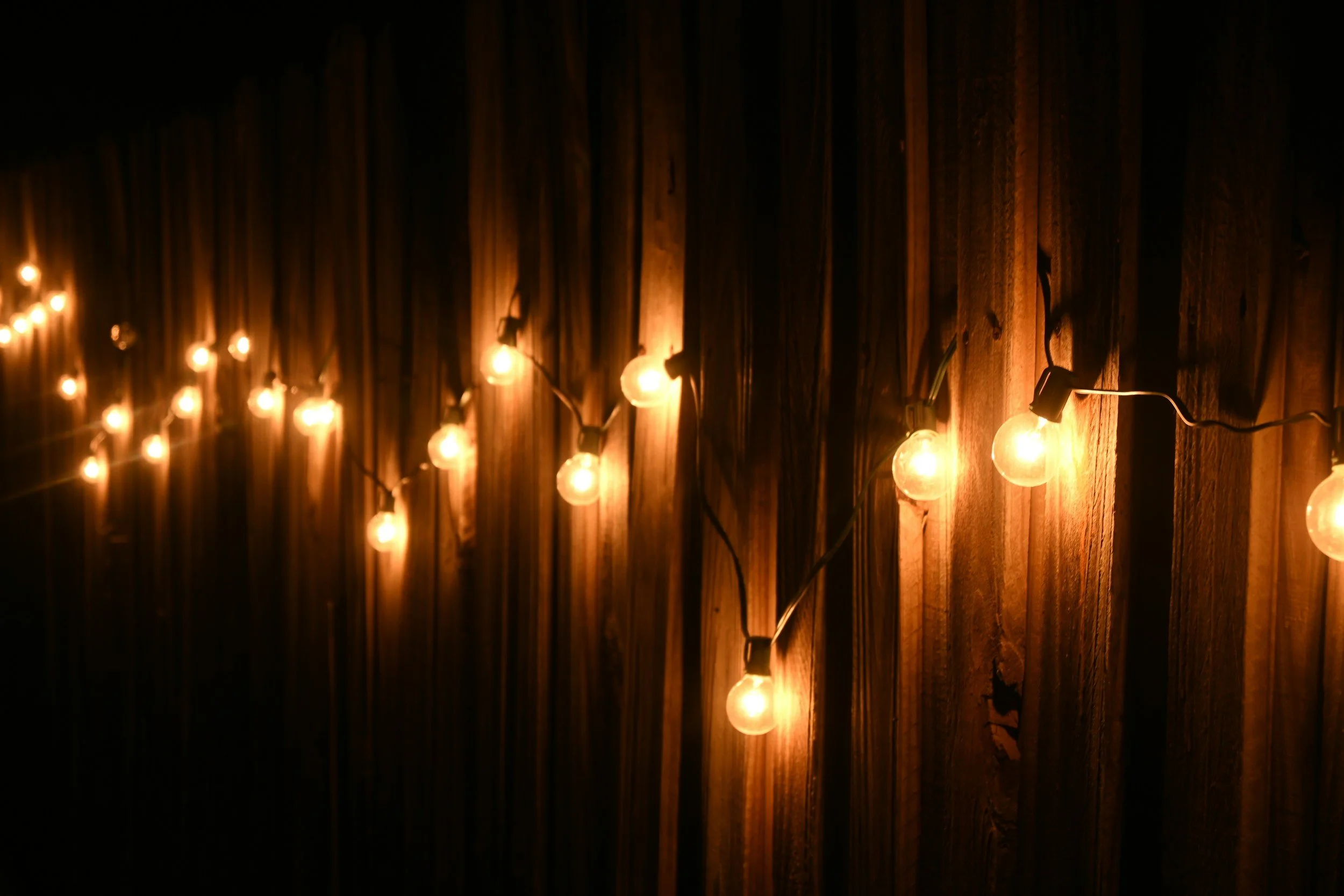 String of warm yellow fairy lights hanging against a wooden wall.