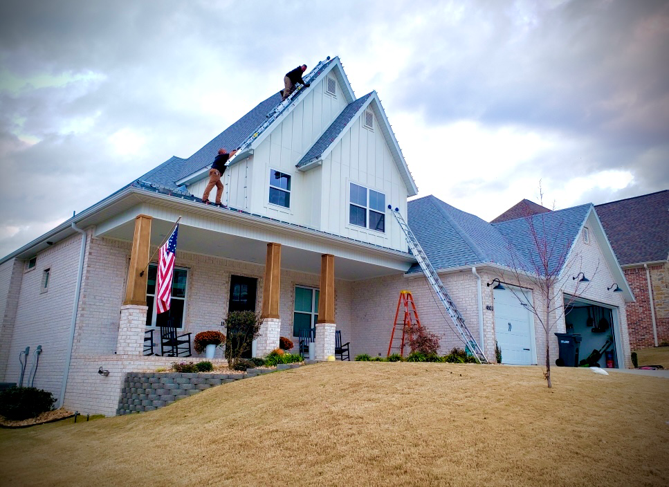 Two workers on the roof of a house installing or repairing lights during daytime.