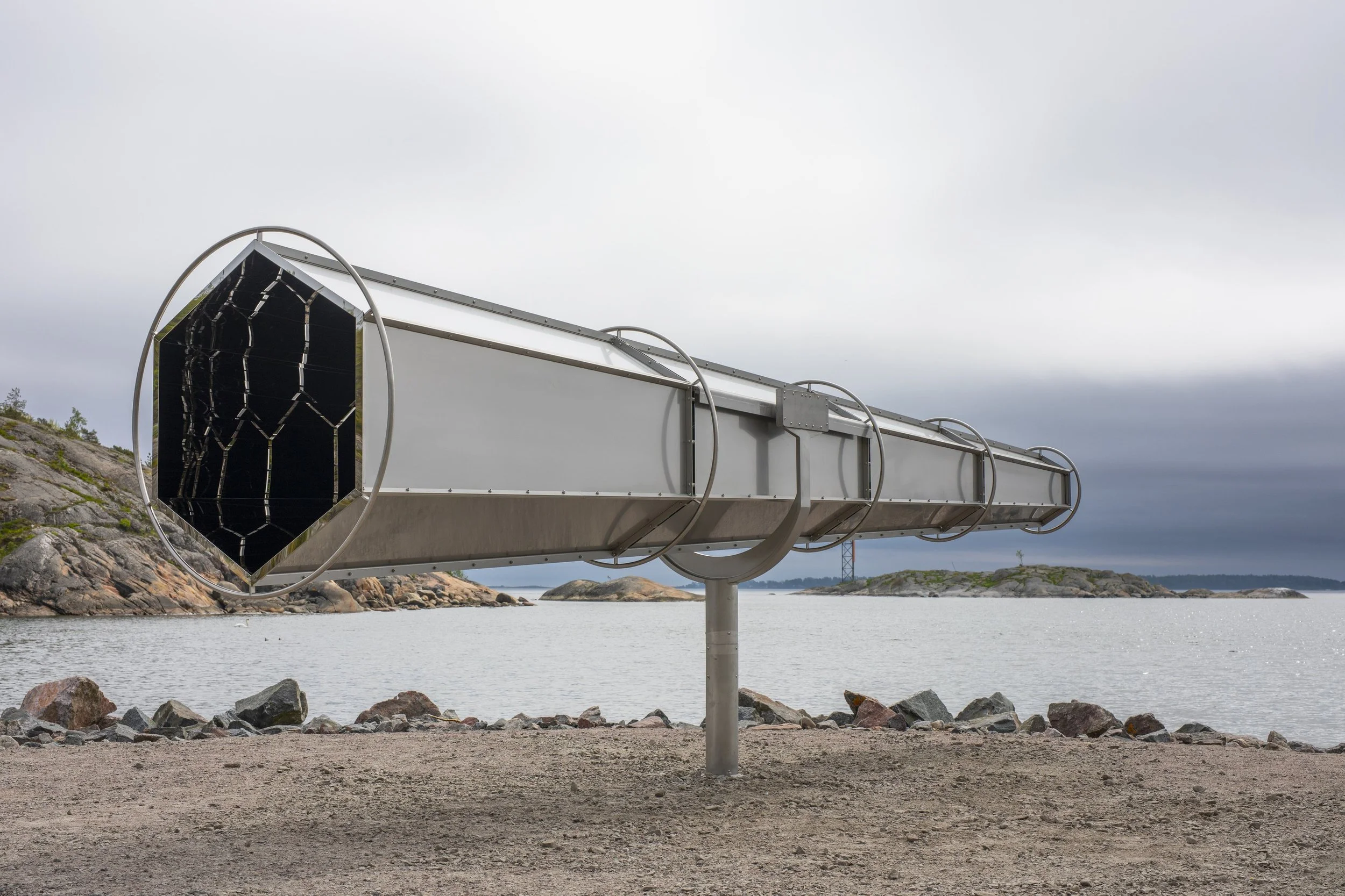 Helsinki Biennial 2025. Olafur  Eliasson, a metallic viewing telescope on a pole facing a body of water with rocky shores and distant islands under a cloudy sky.