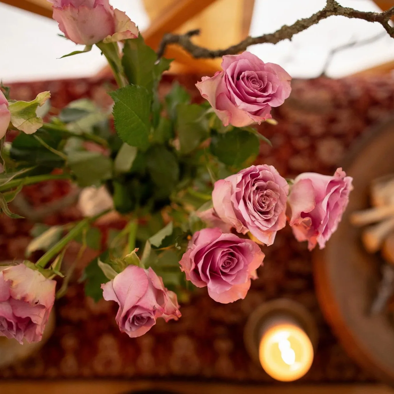 Cluster of pink roses with green leaves indoors with patterned carpet and a ceiling light visible.