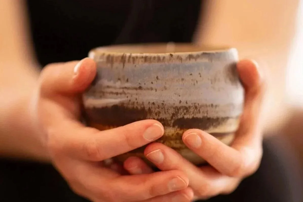 A person with fair skin holding a rounded, striped ceramic bowl with both hands