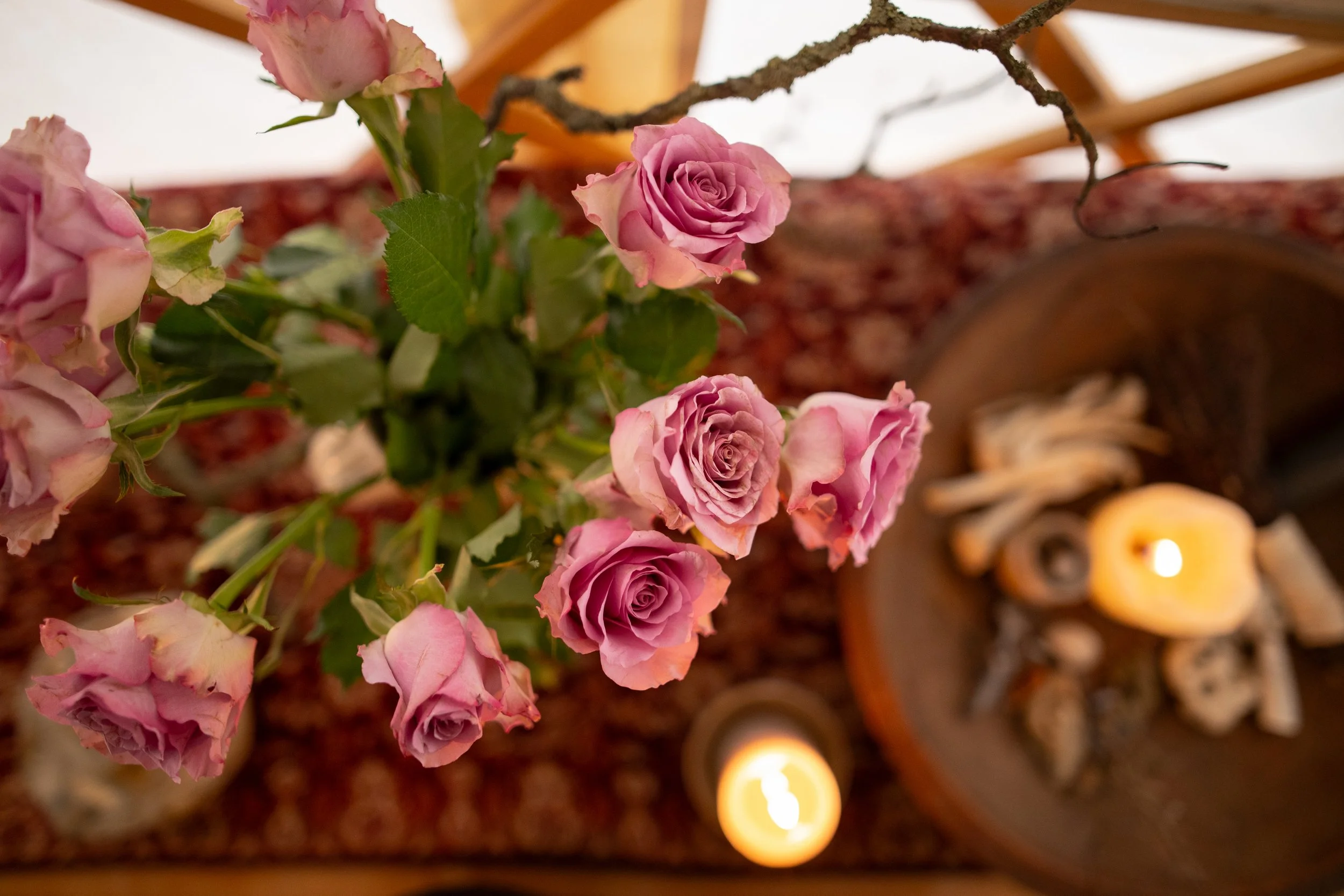 Pink roses in a vase with candles and pinecones arranged on a table.