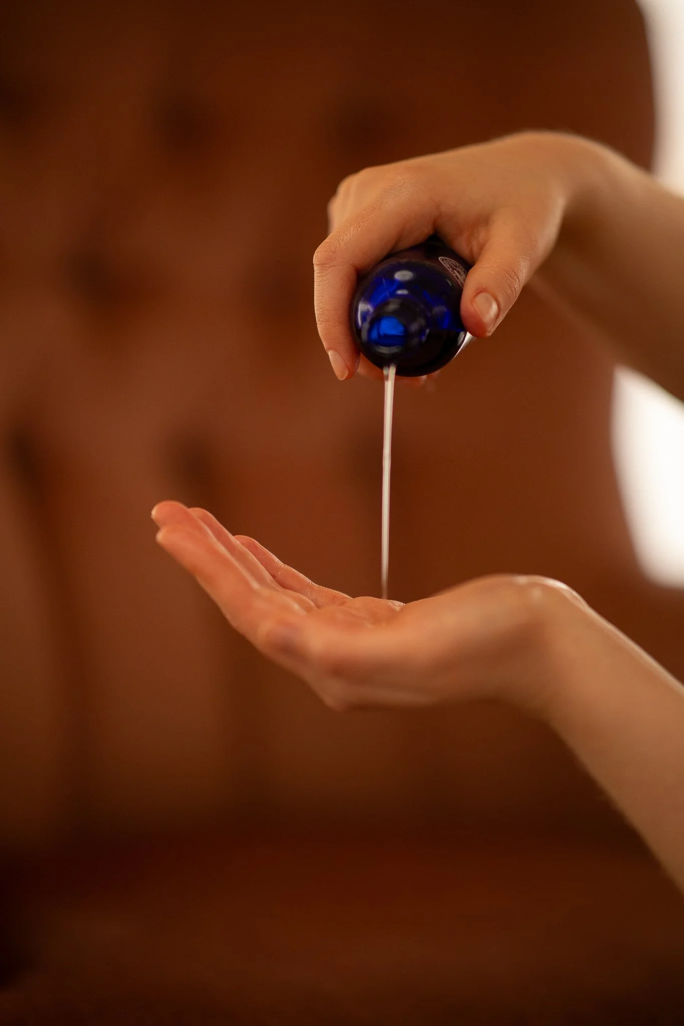 Person pouring lotion or oil from a blue bottle onto their palm.