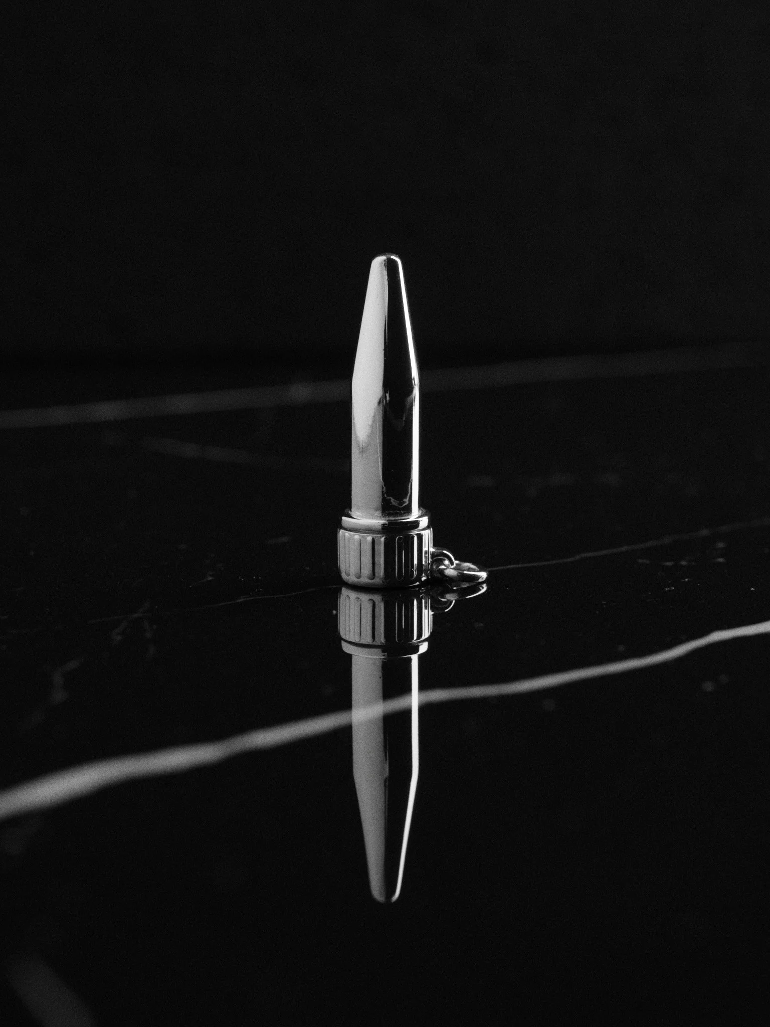 Ein silberner Kugelschreiber mit einem Ankermotiv, der auf einer schwarzen Oberfläche liegt, deren Spiegelung sichtbar ist.