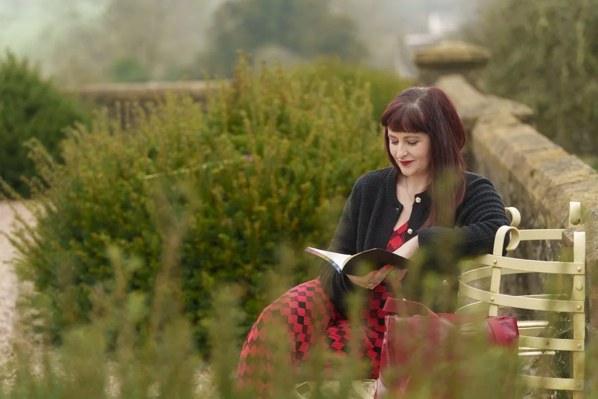 Elin sitting on a park bench, reading a notebook, with blurred greenery around her.