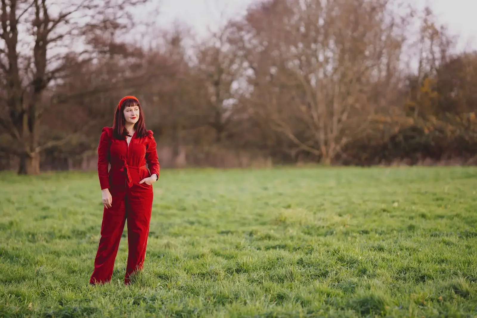 Elin Edwards, a woman with dark hair wearing a red jumpsuit, stands in a grassy field with trees in the background.