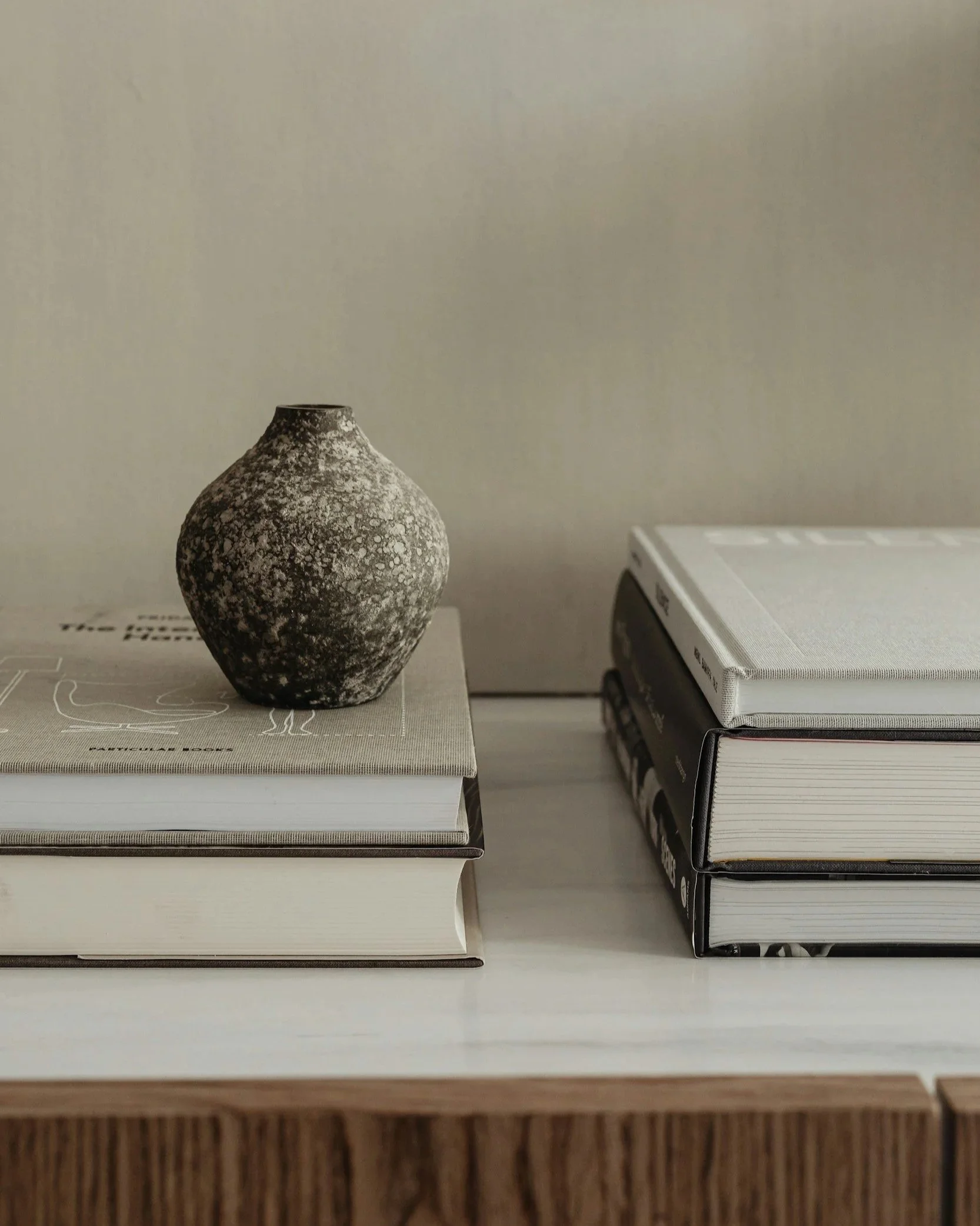 A ceramic vase with a speckled pattern sits on top of two stacked hardcover books, placed on a wooden surface, with a plain background.
